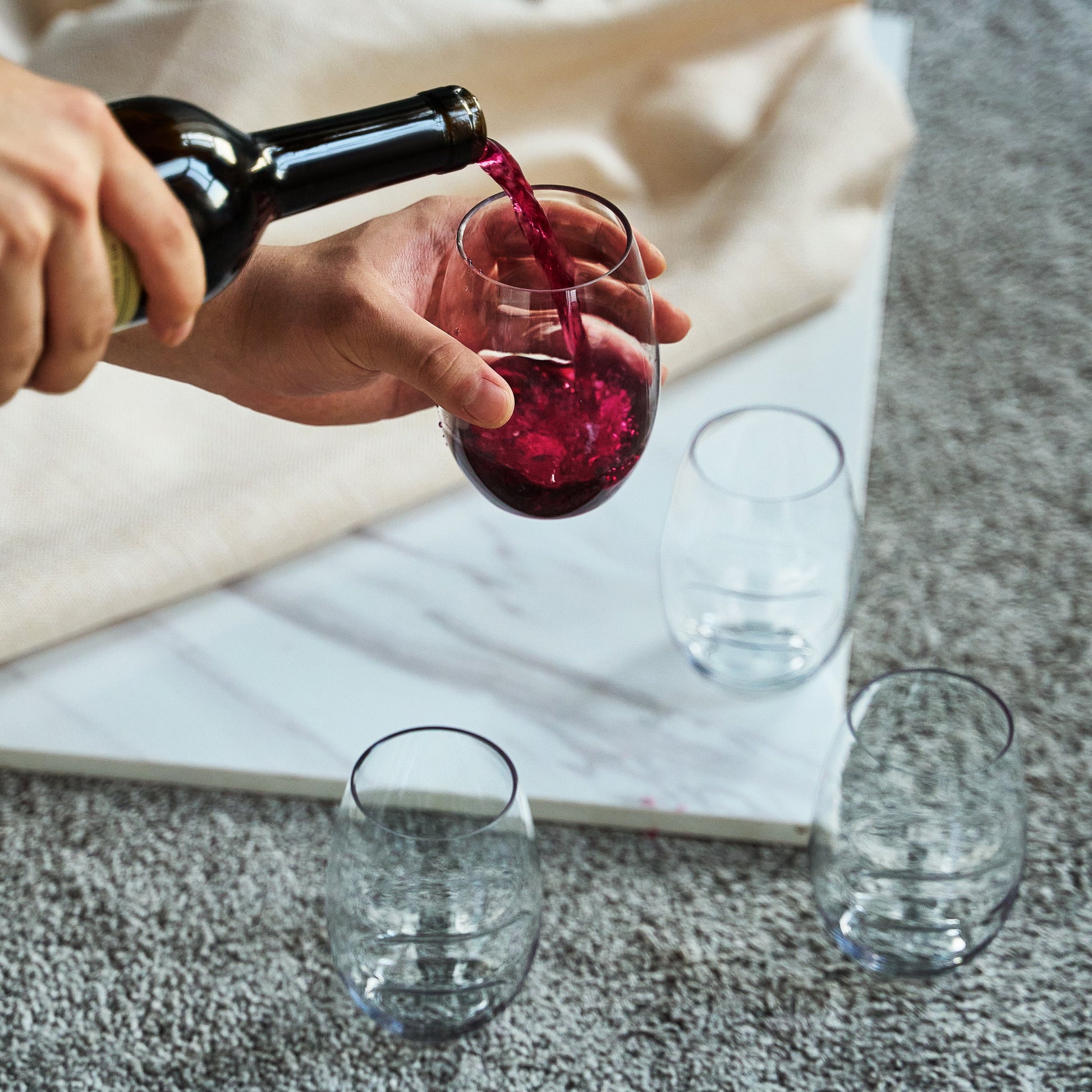Stemless finger-indent wine glass being filled, clear acrylic, with red wine