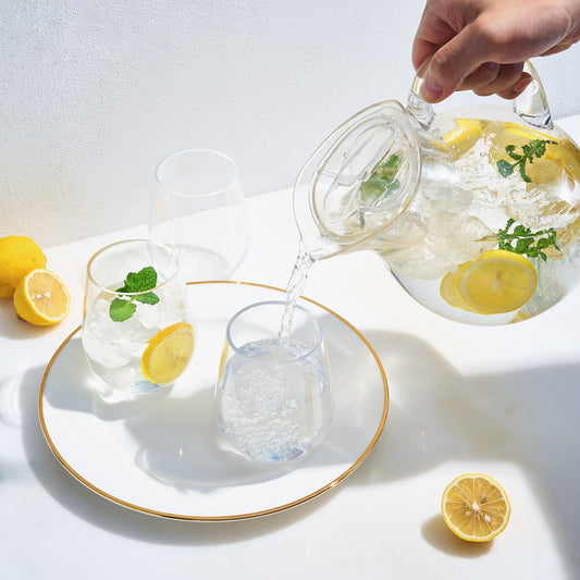 Clear acrylic pitcher pouring water into a glass, with lemon slices and mint
