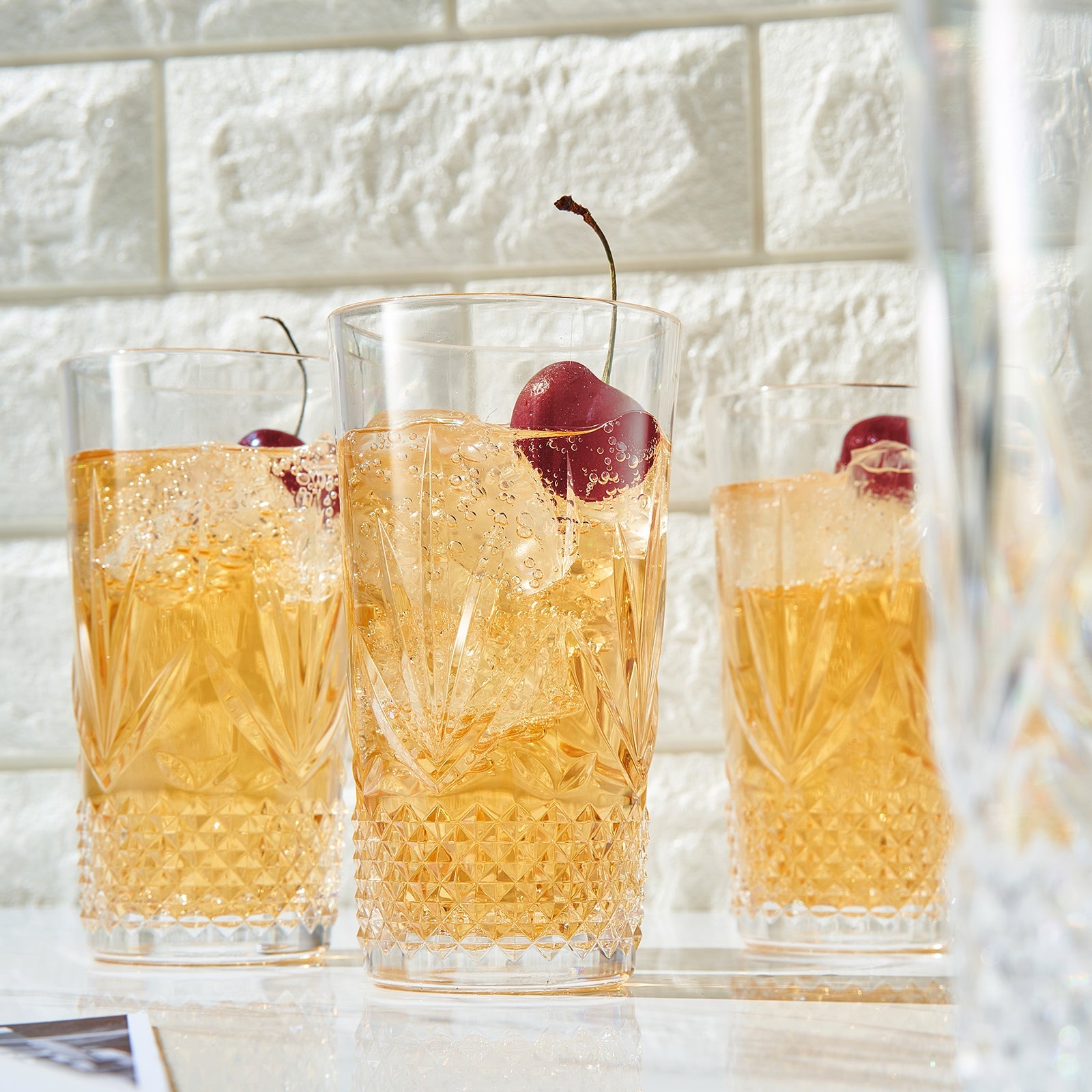 Faceted acrylic highball glasses filled with amber drink, ice and red garnish