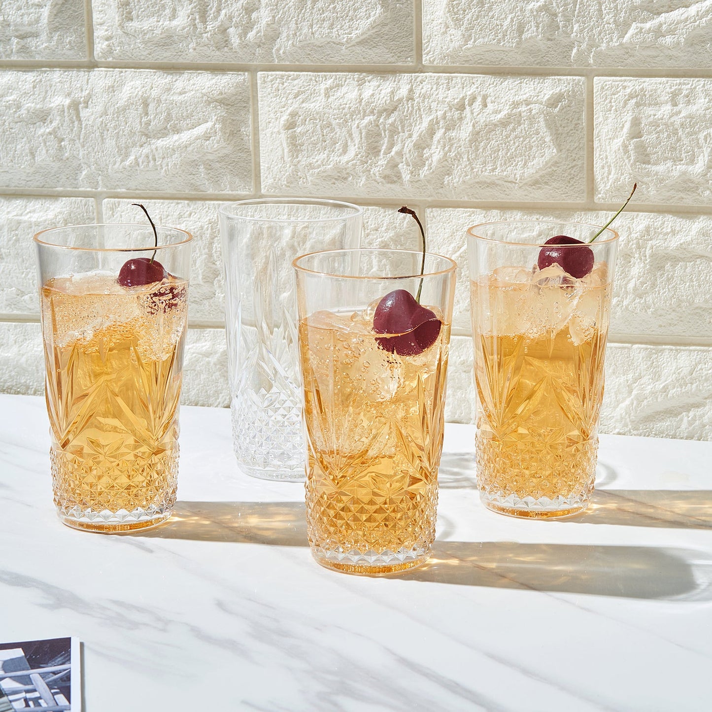 Faceted acrylic highball glasses filled with amber drink, ice and red garnish