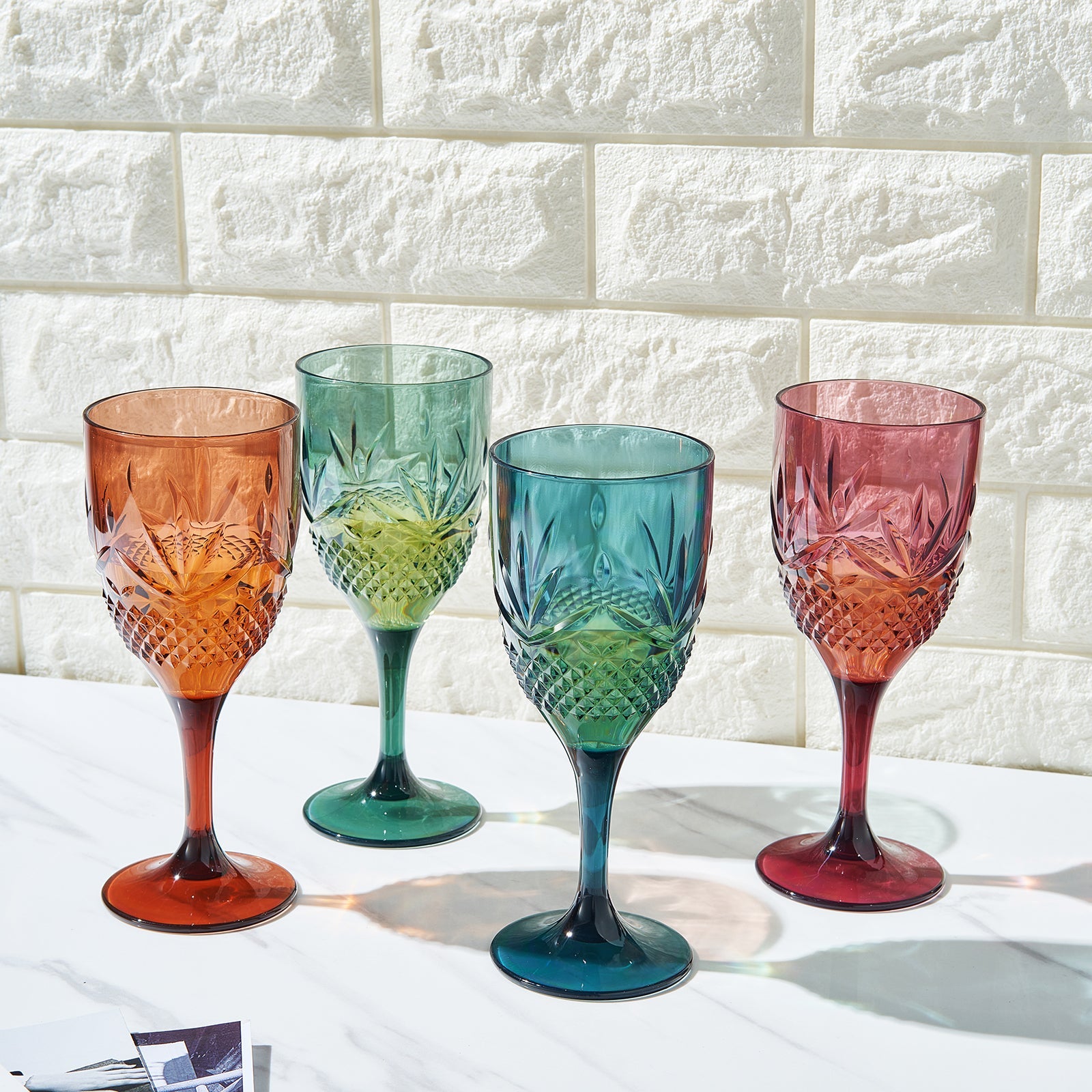 Set of four stemmed wine glasses with faceted bowls in orange, green, teal, and red