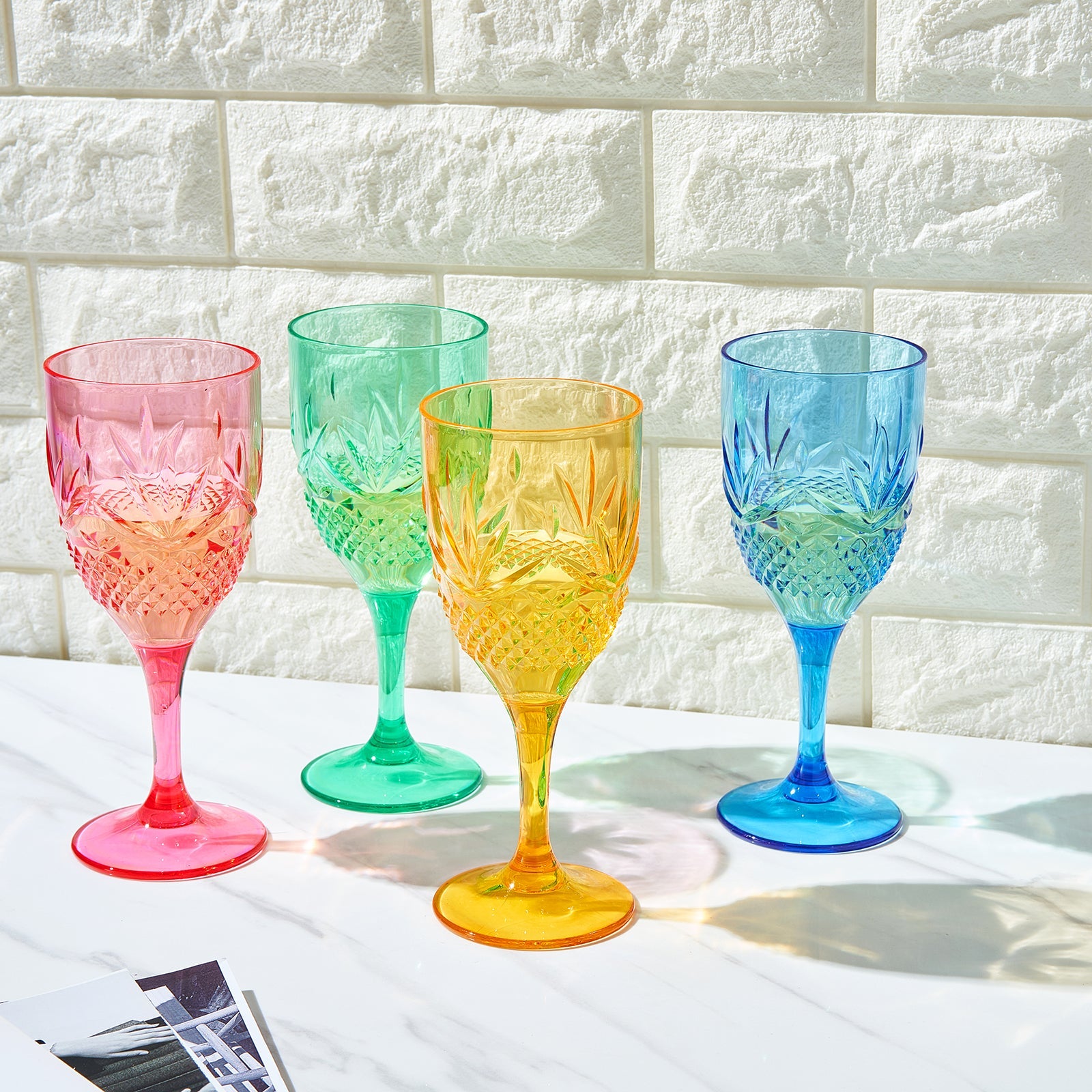 Four stemmed acrylic wine glasses with faceted diamond pattern; pink green yellow blue