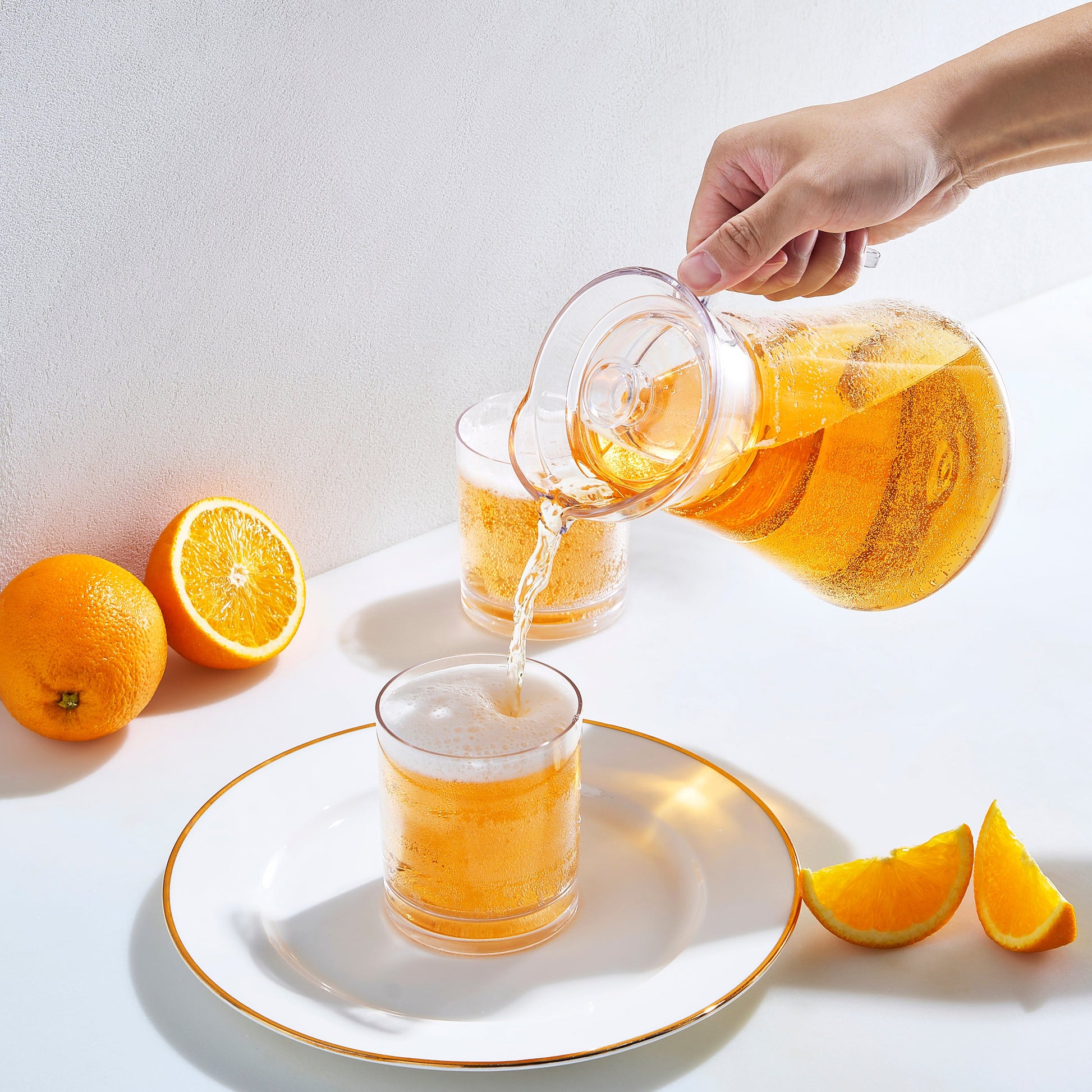 Acrylic pitcher pouring orange drink into a glass; clear pitcher with lid.