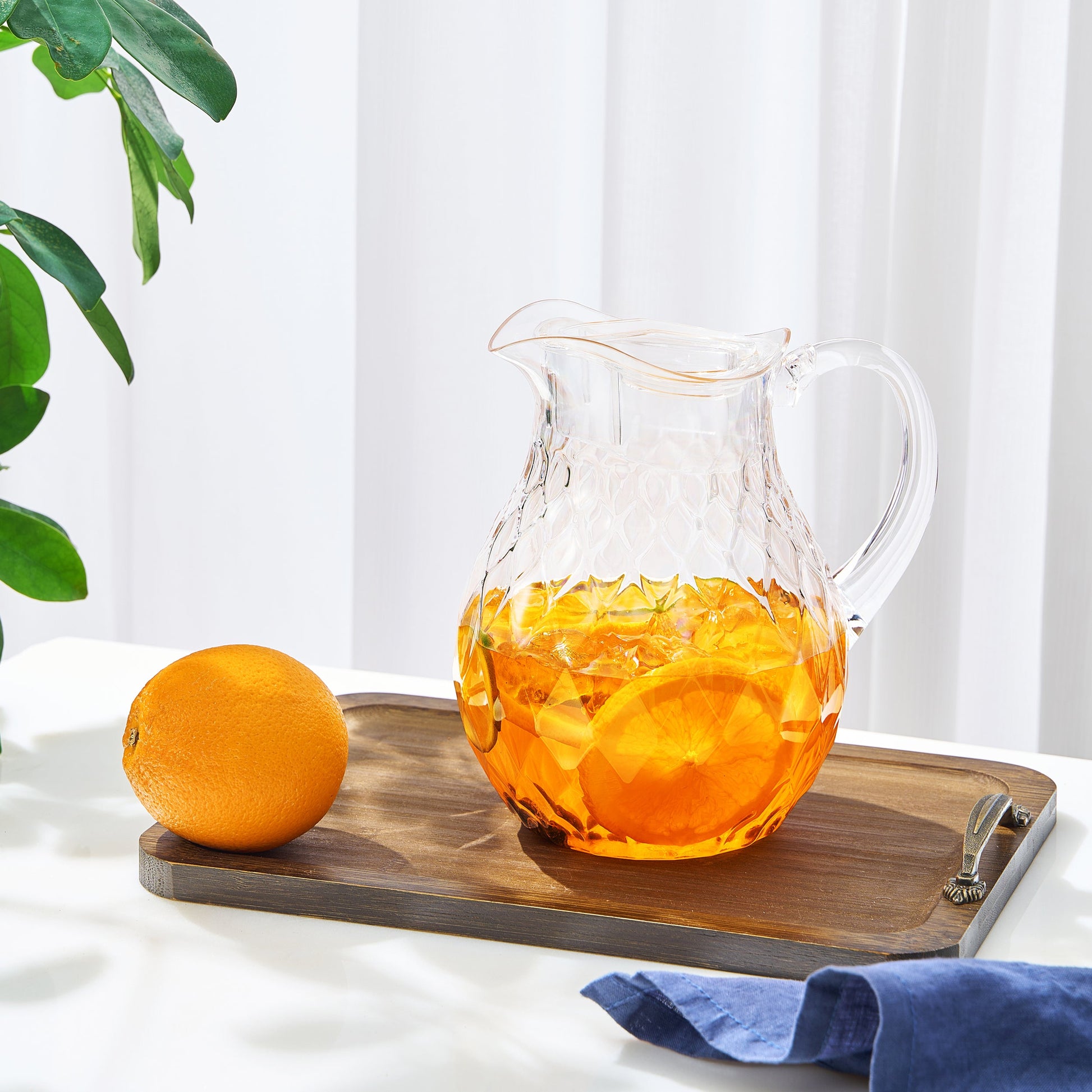 Acrylic pitcher with clear handle and diamond pattern, filled with amber citrus beverage