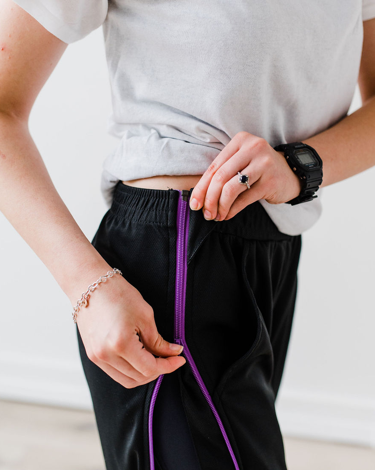 Person tying a purple shoelace on black pants with a neutral background