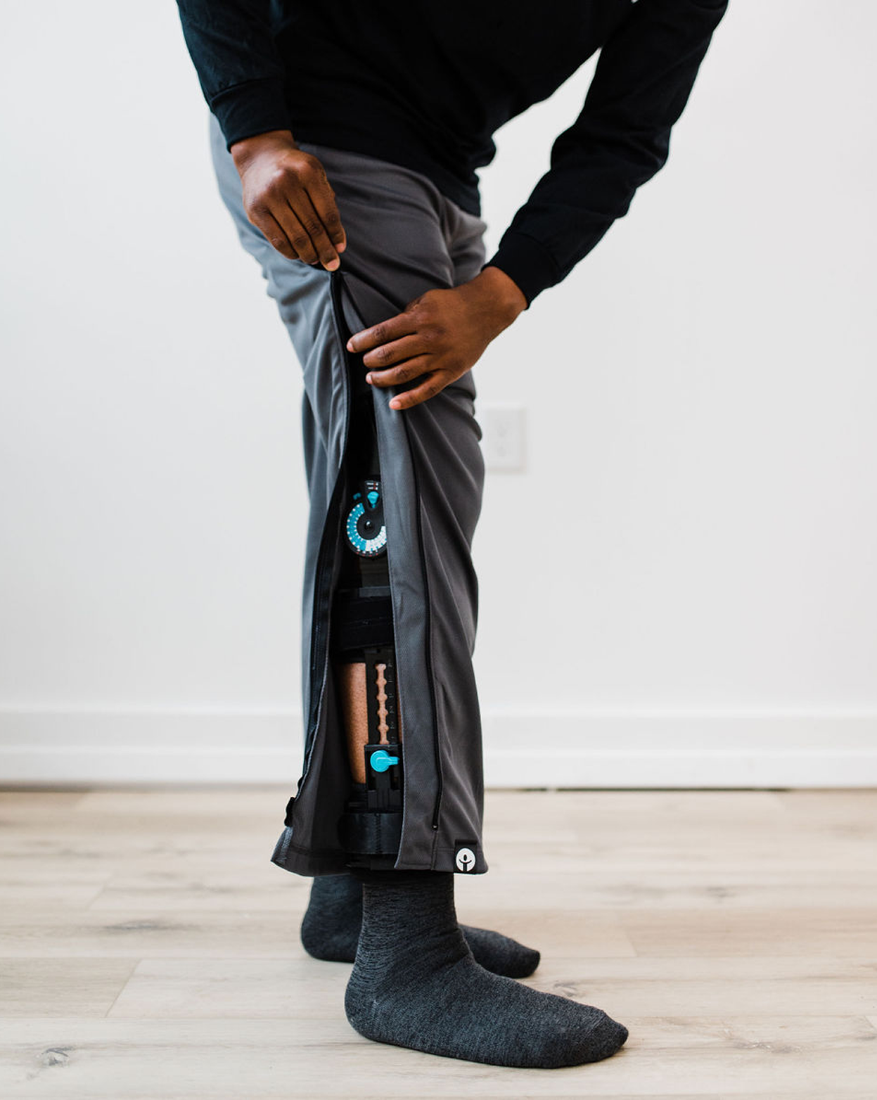 Person wearing gray pants with a visible brand logo on a light wooden floor.