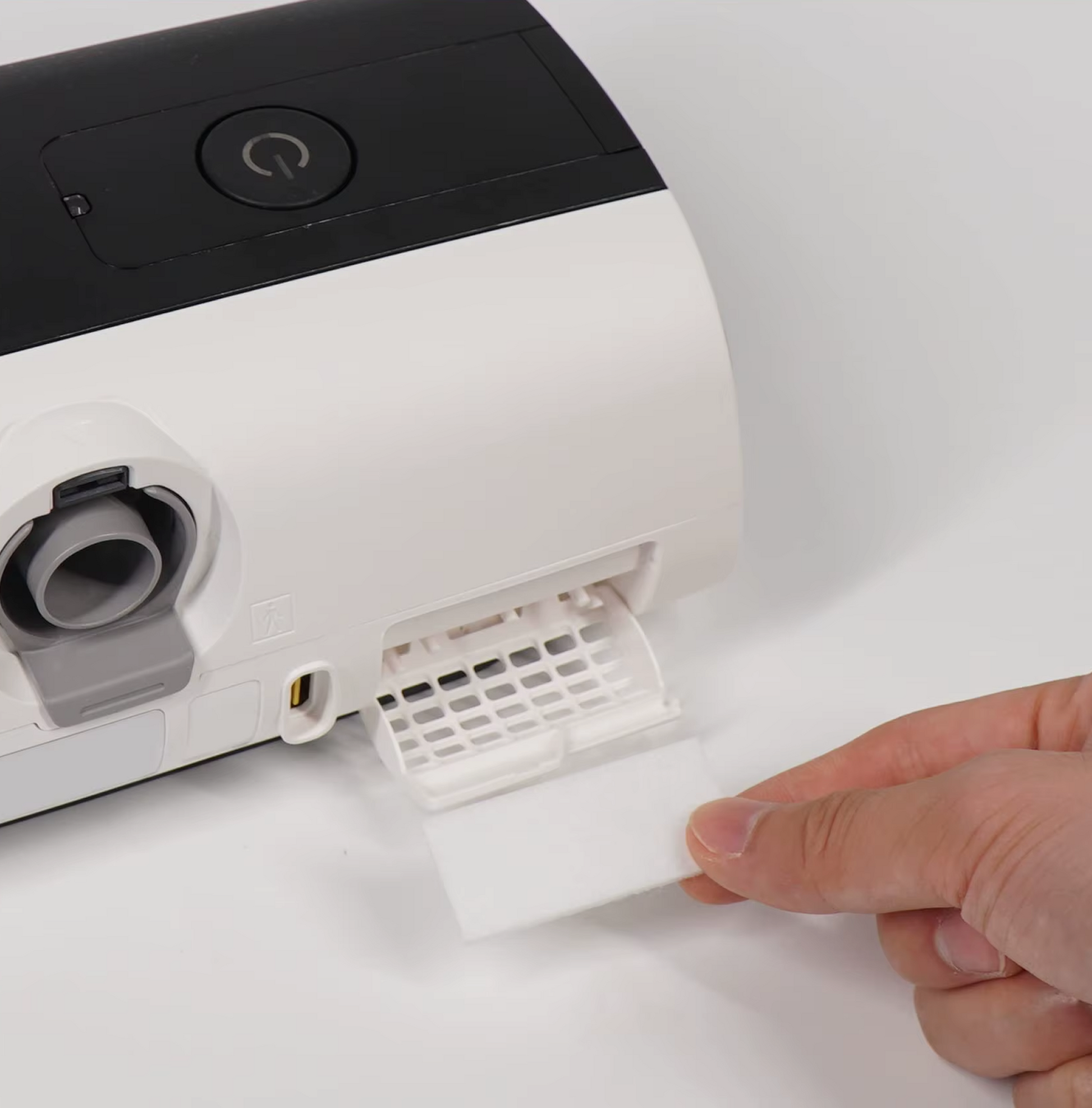 A hand inserts a white AirSense 11 Filter Pack into the filter compartment of a white and black ResMed AirSense 11 device.
