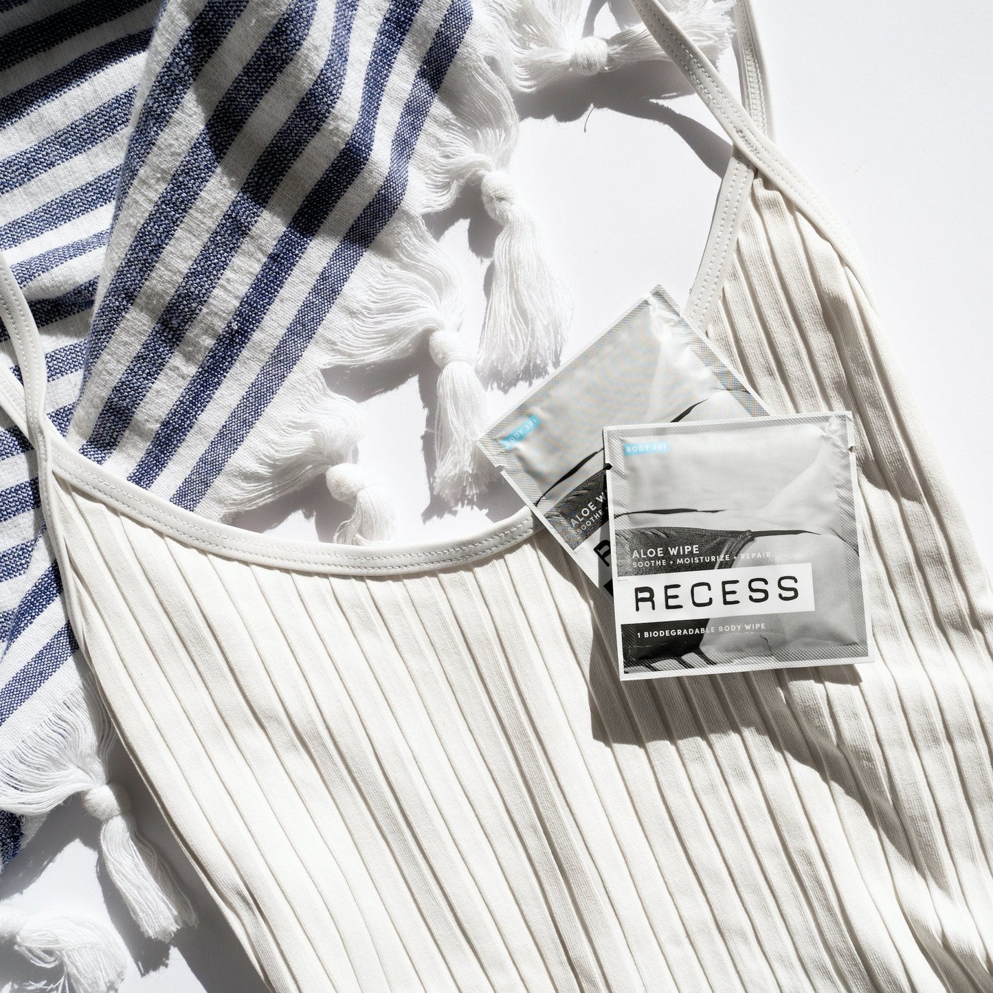 Two packages of Recess wipes on a white textured surface with a striped towel.