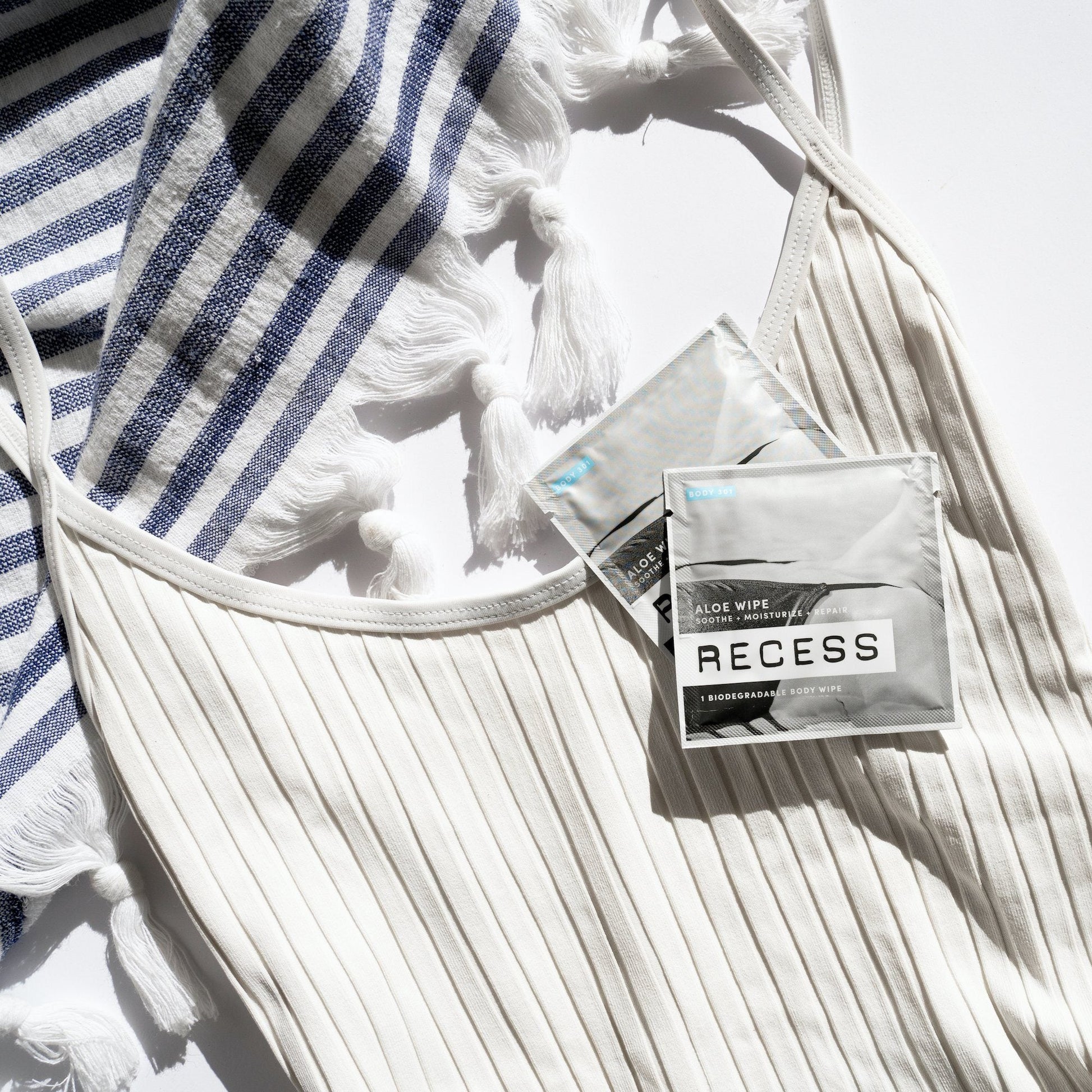 Two packages of Recess wipes on a white textured surface with a striped towel.