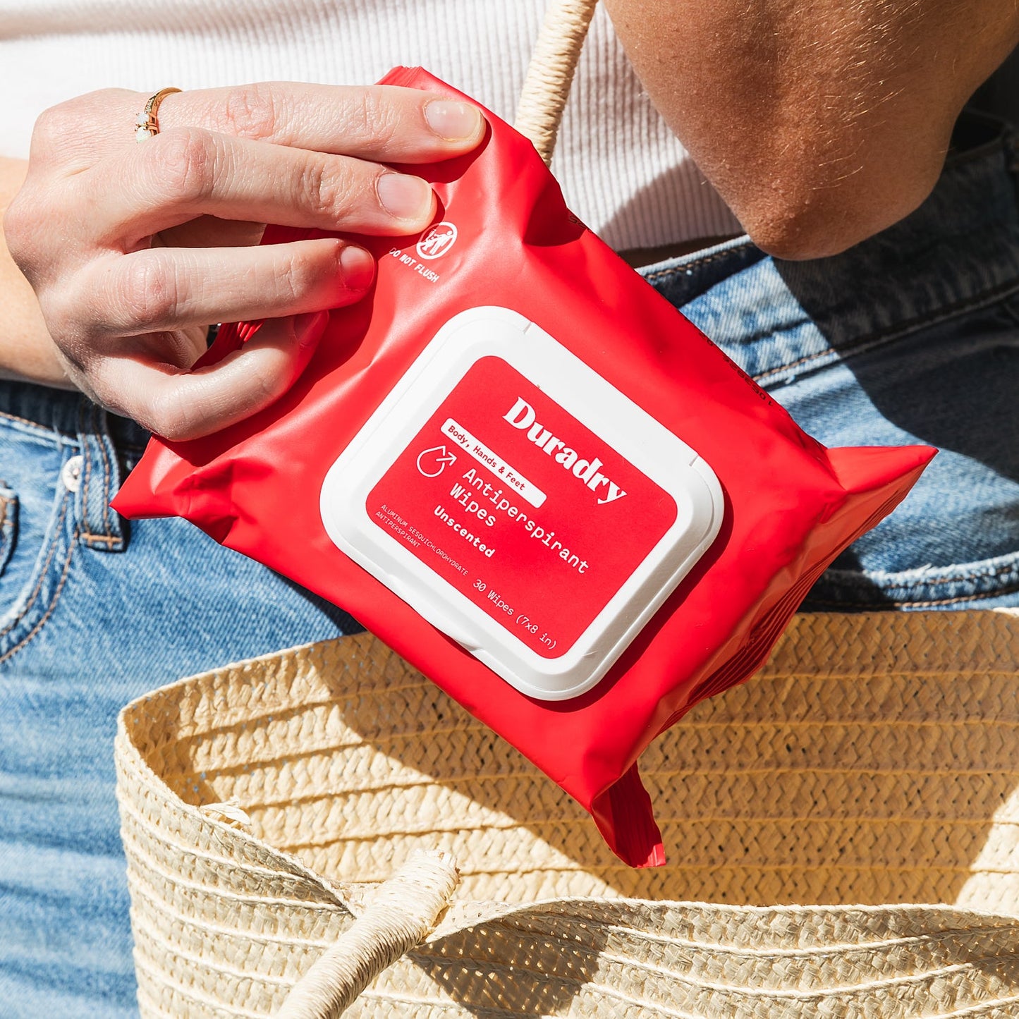 Red package of Durady antiperspirant wipes held by a person with a straw bag in the background.