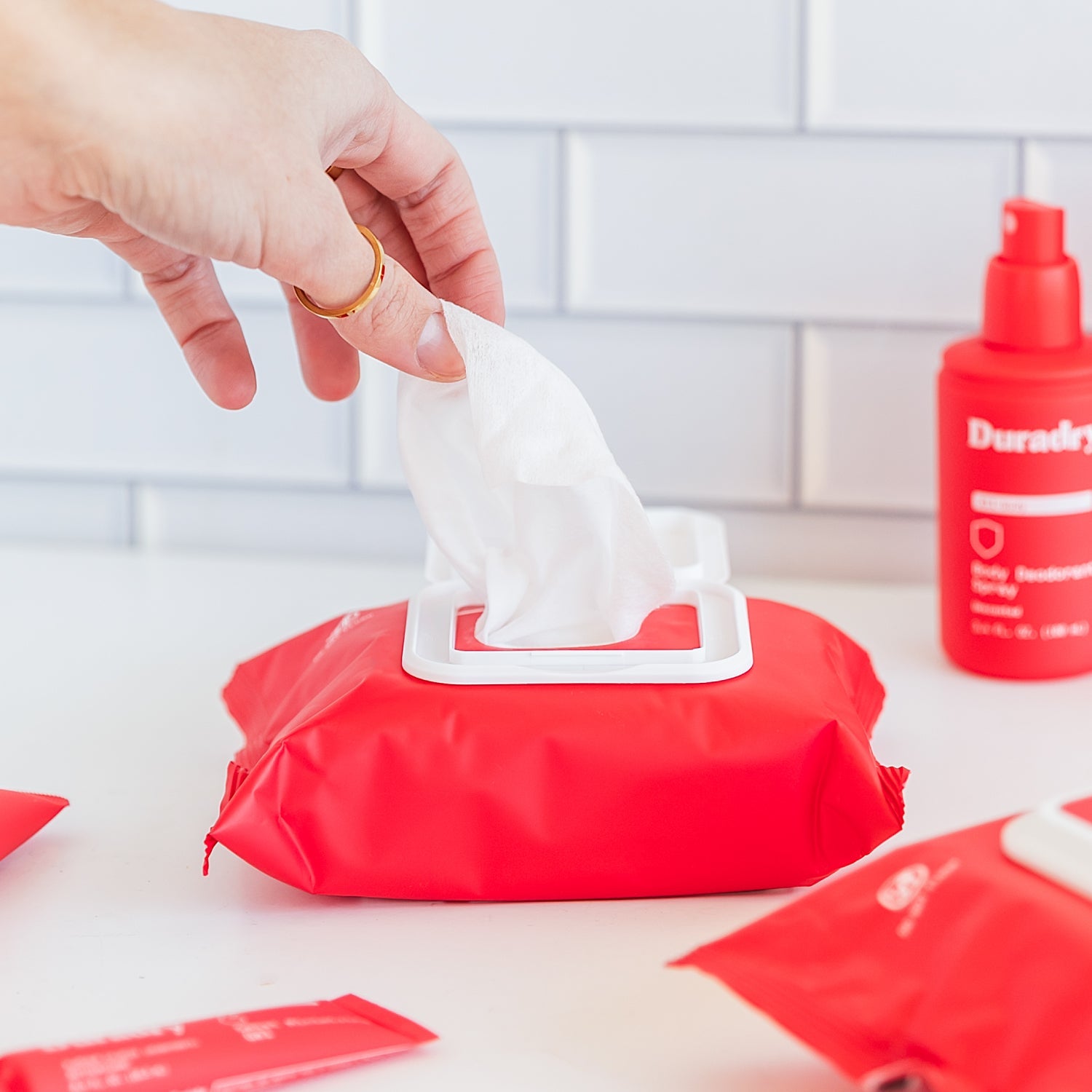 Hand reaching for a tissue from a red tissue pack with a bottle of Duracil in the background.