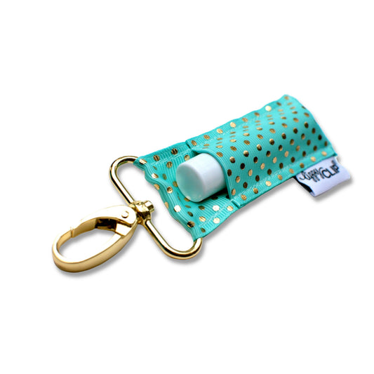 Teal keychain with gold accents and a small white container on a white background