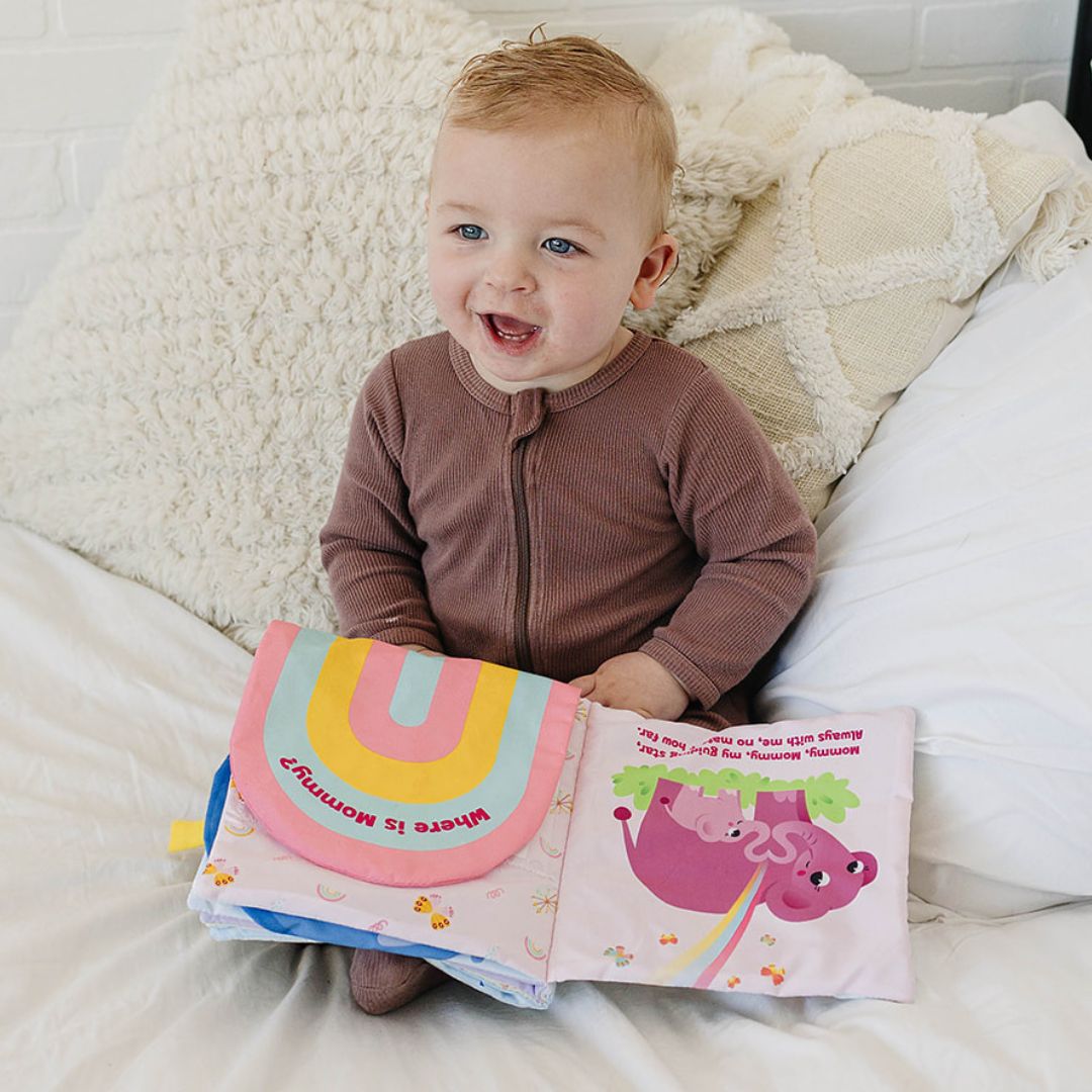 Baby holding a cloth storybook with animal illustrations and pink-and-blue fabric covers.