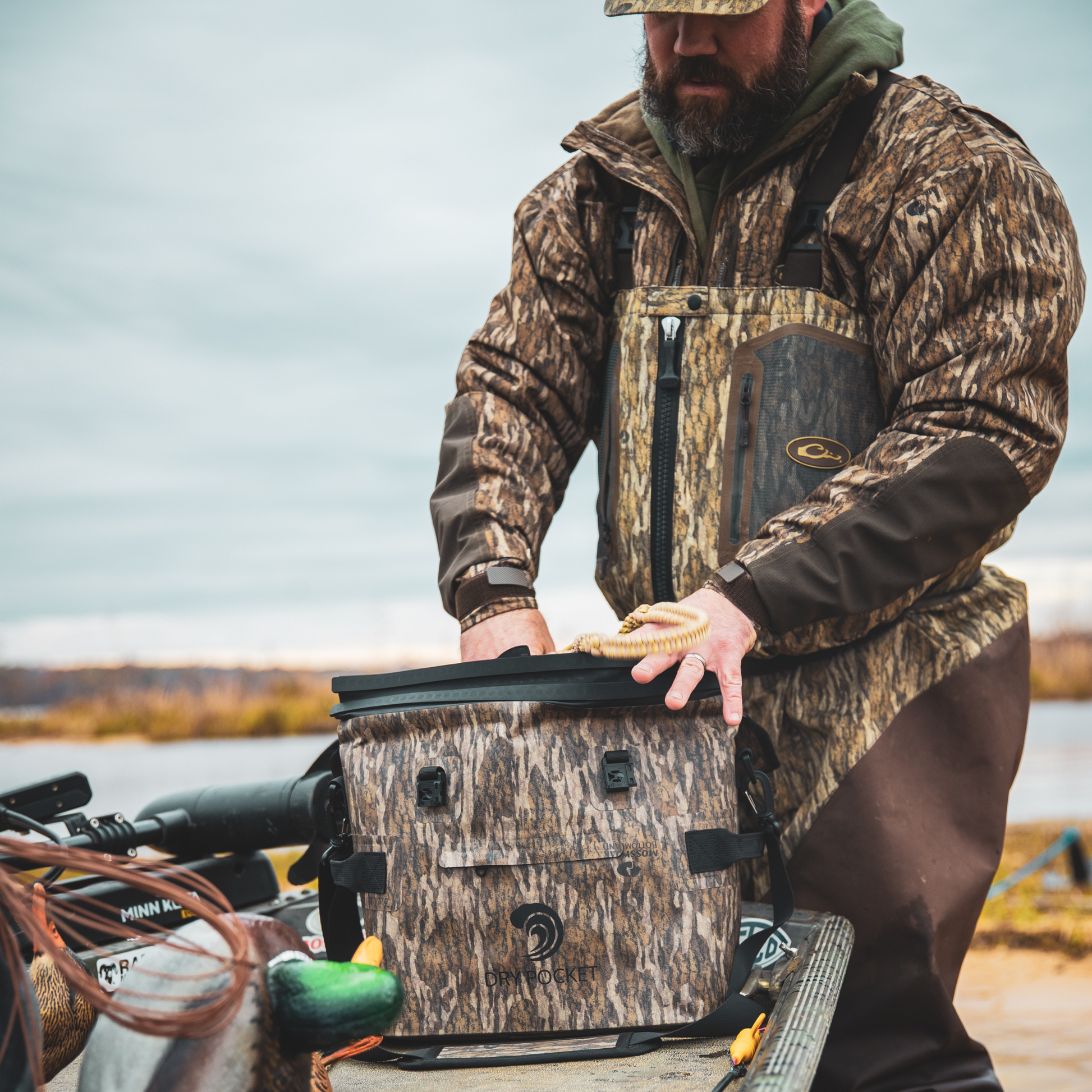 Waterproof floating cooler bag in Mossy Oak camo with black straps, held by a person