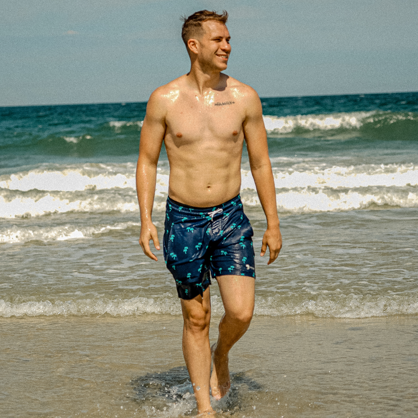 Men's dark swim shorts with teal palm tree print and white drawstring waist