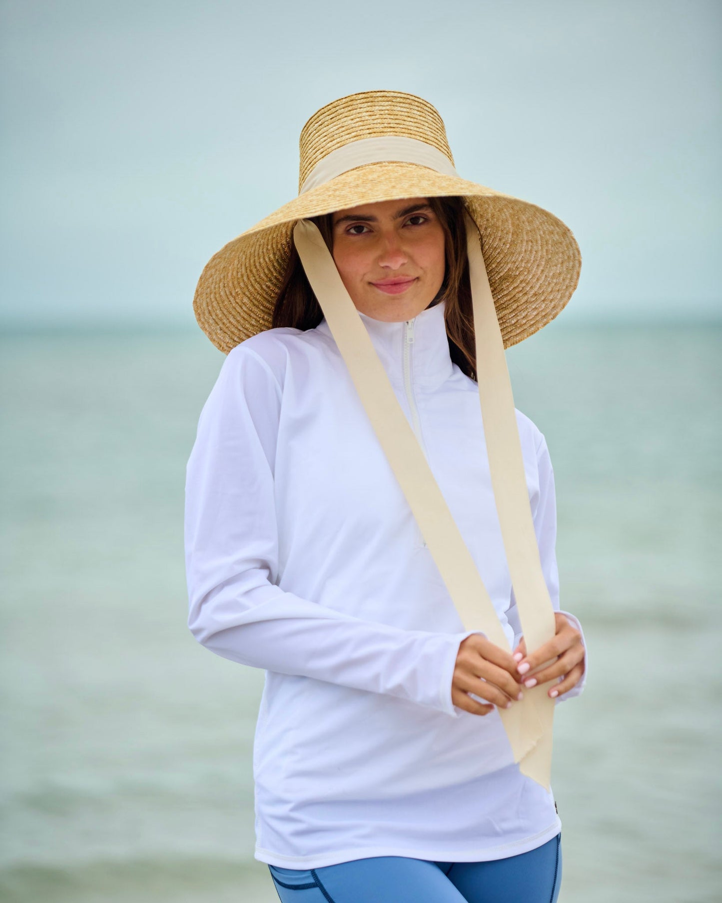Capri sun hat in straw with wide brim, white band, and long ties hanging down.
