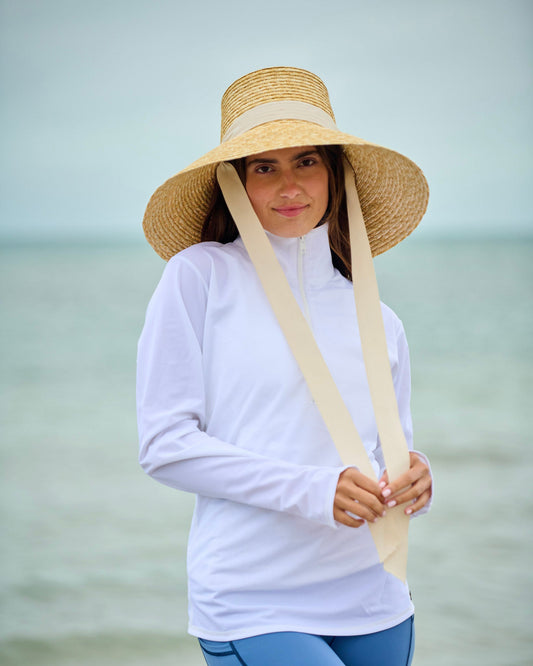 Capri sun hat in straw with wide brim, white band, and long ties hanging down.