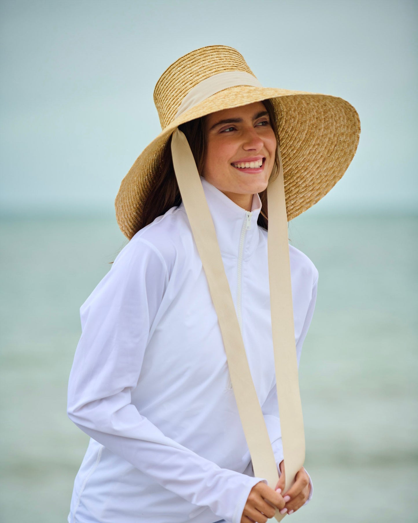 Capri sun hat in straw with wide brim, white band, and long ties at front.