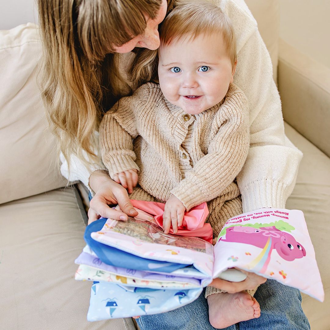 Cloth storybook with colorful covers and animal illustrations, held by an adult and baby.