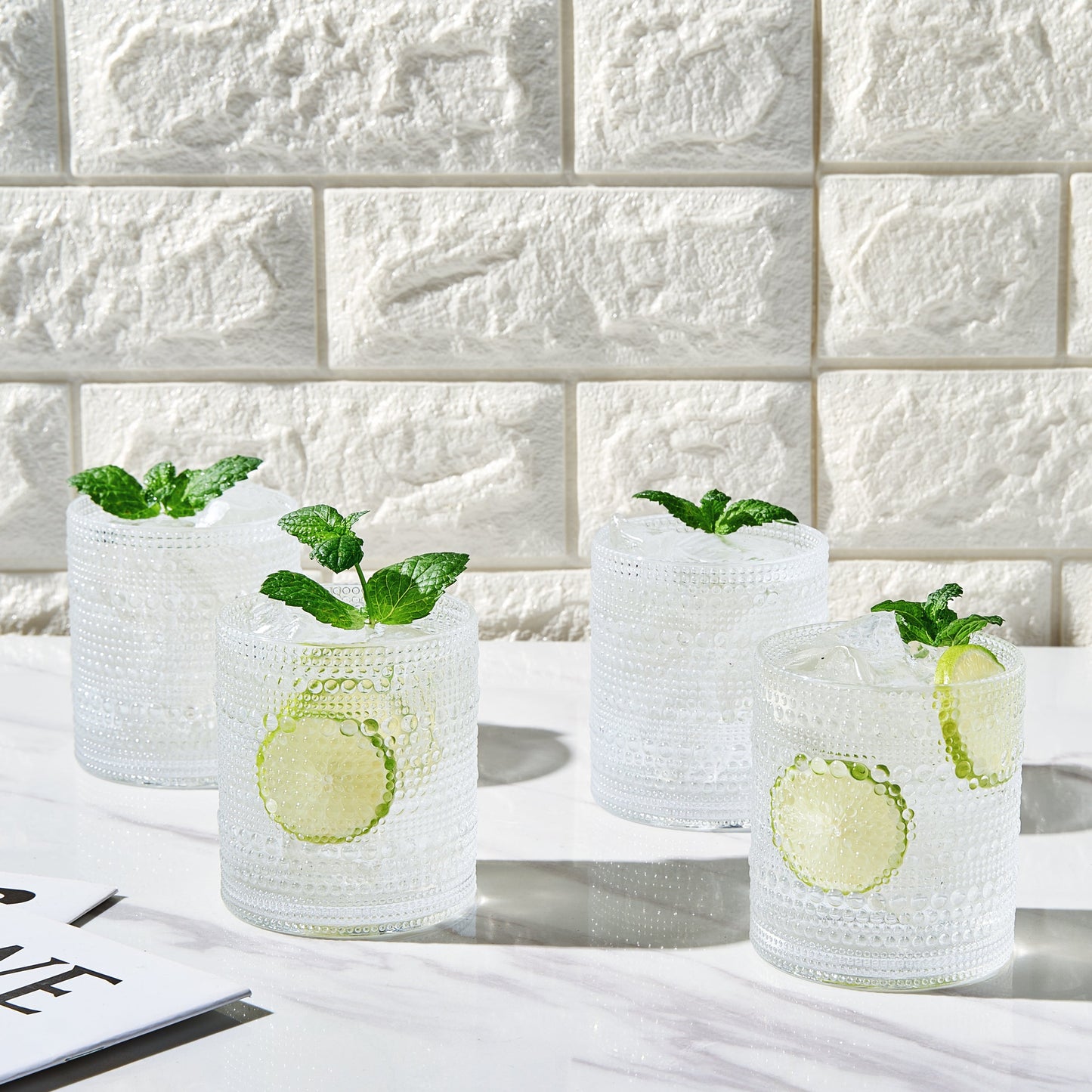 Four clear acrylic hobnail lowball whiskey glasses with raised dotted pattern on sides