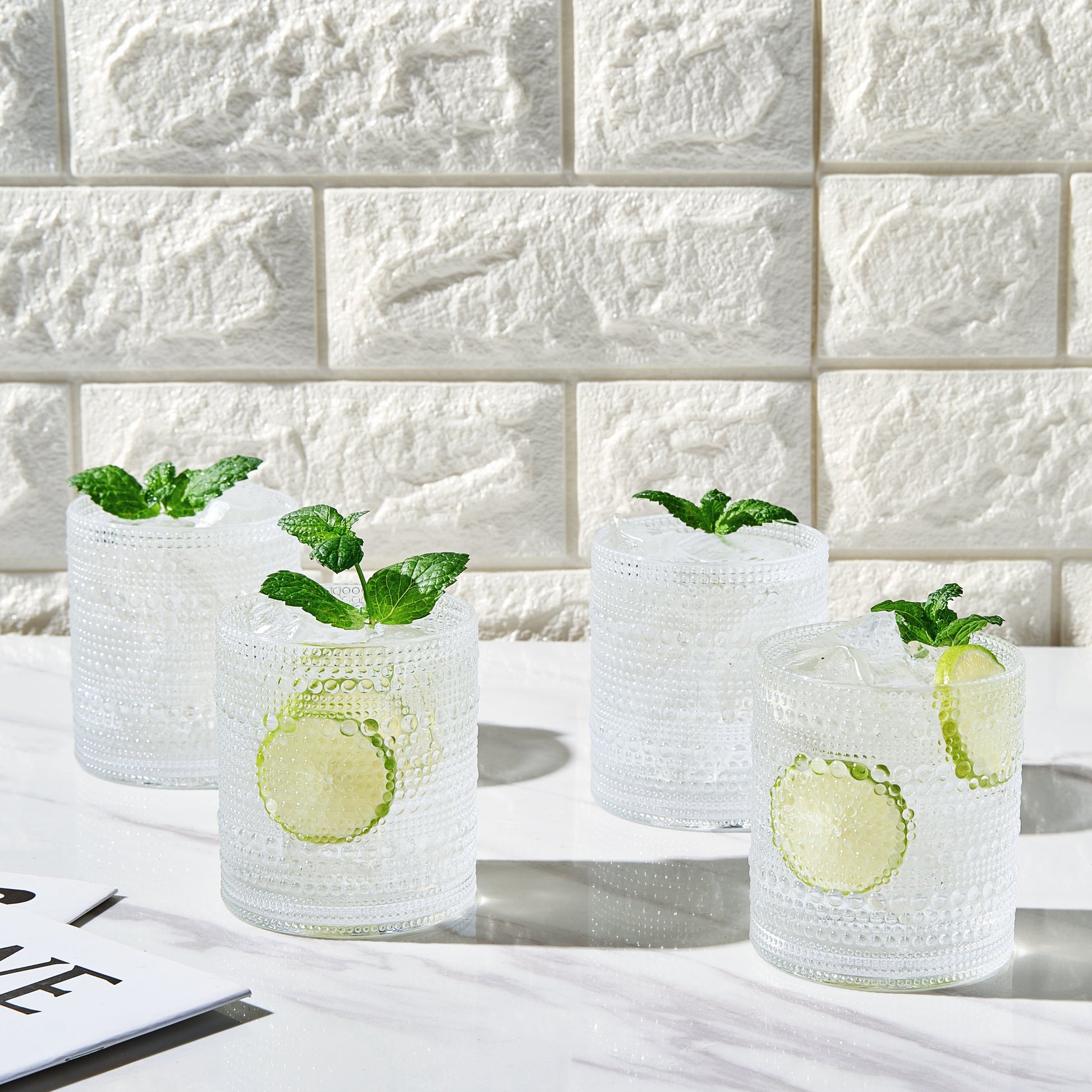 Four clear acrylic hobnail lowball whiskey glasses with raised dotted pattern on sides