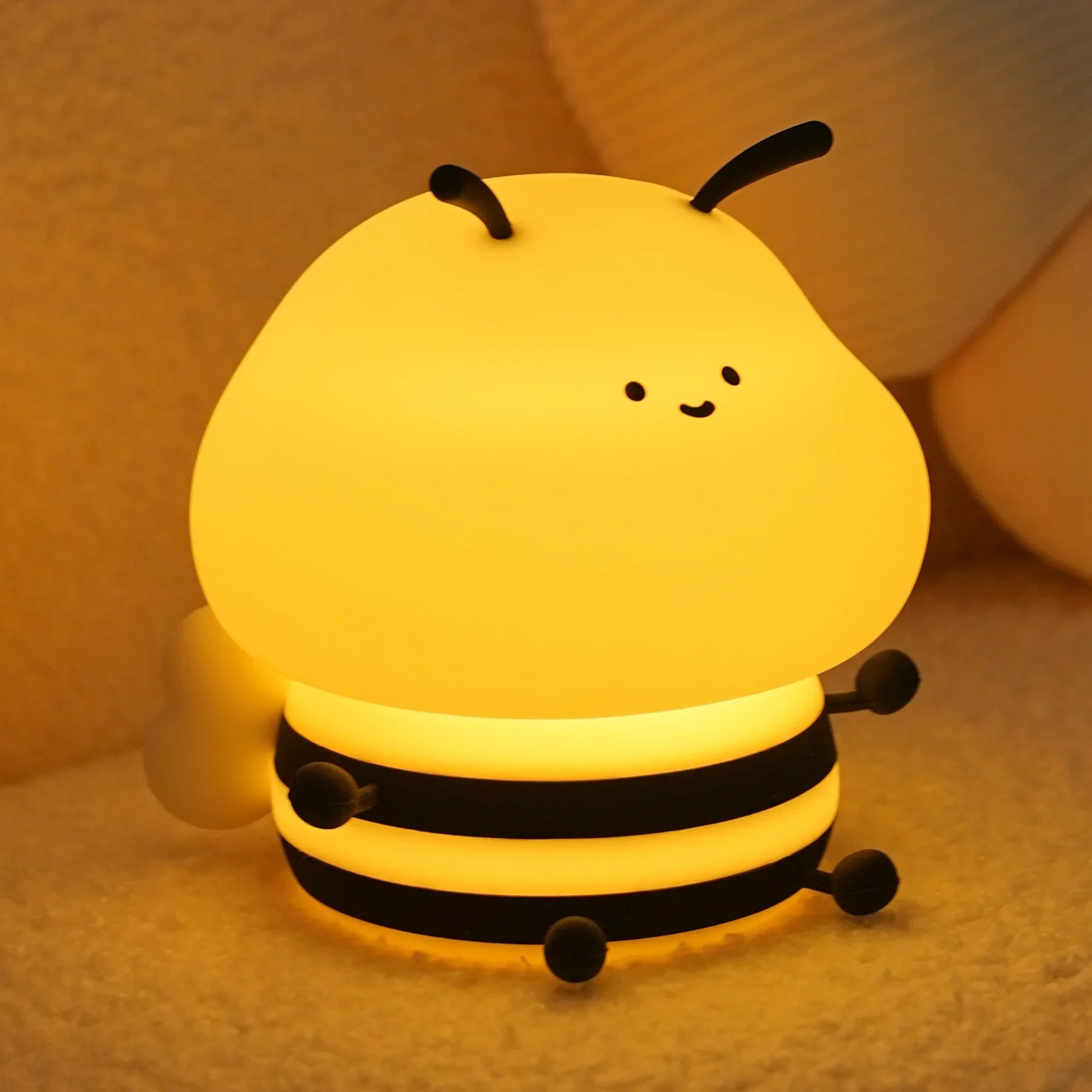 Bee night light with smiling face, warm yellow glow, and three black ring layers on floor