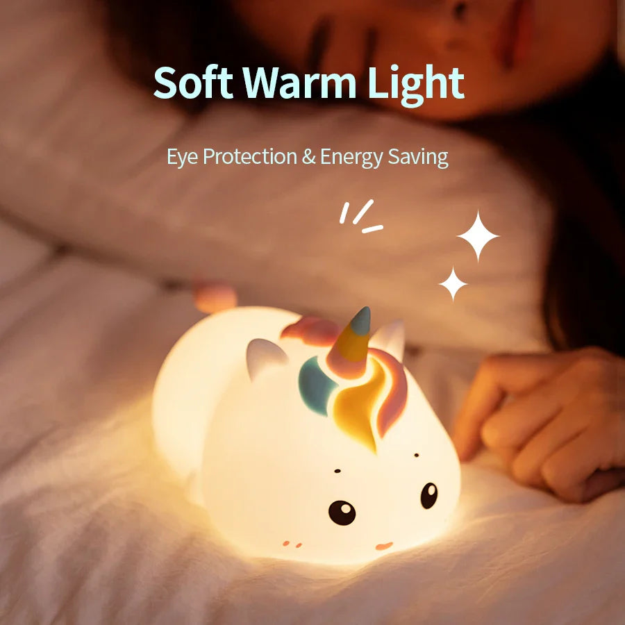 Warm glowing unicorn night light on a bedspread, cute horned face.