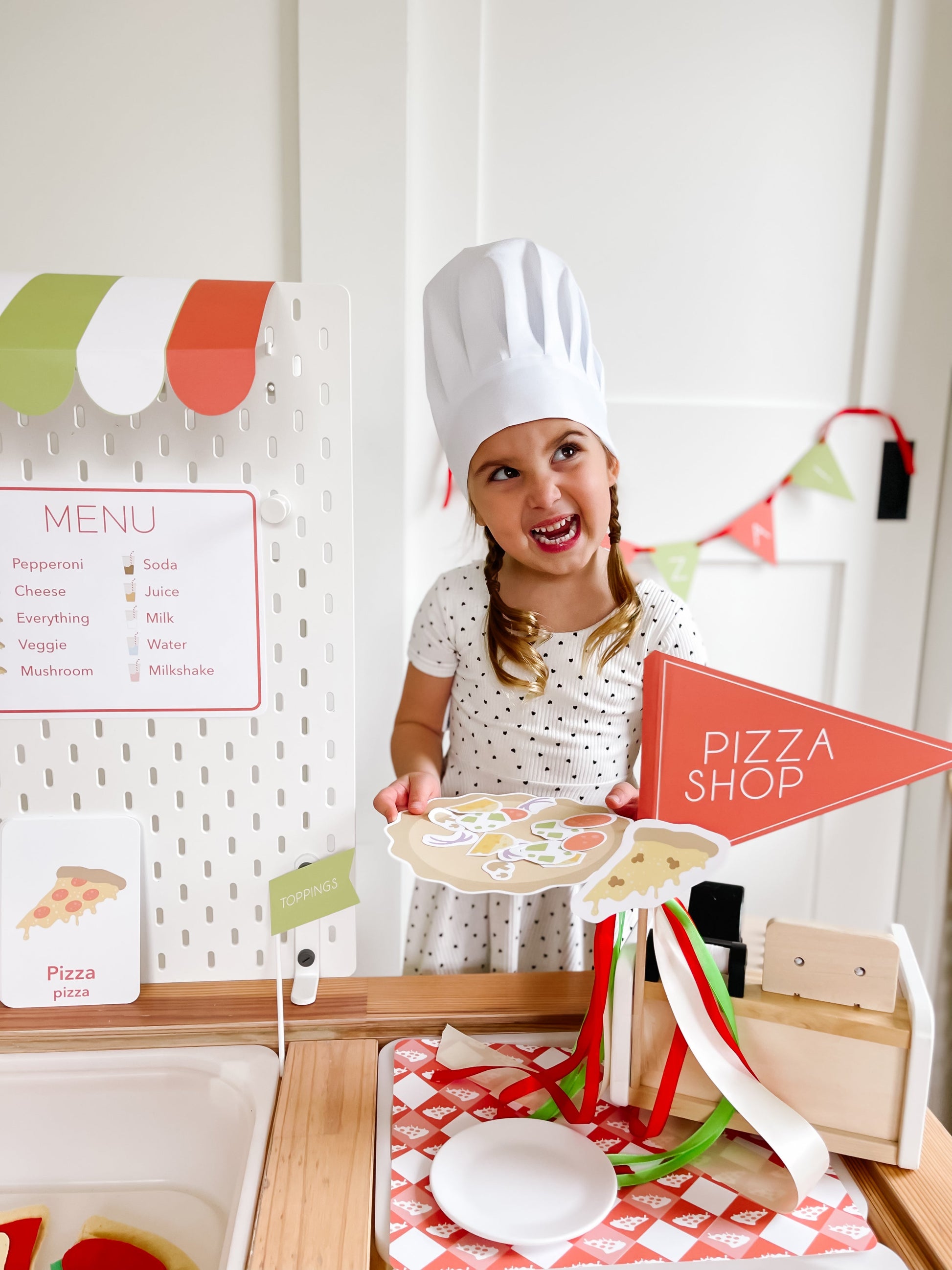 Pizza shop play kit with child in chef hat holding pizza cutouts and toppings