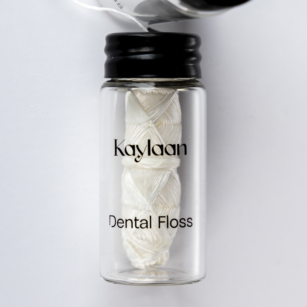 Dental floss bottle close-up with Kaylan label and white floss strands in glass