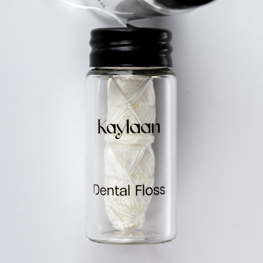 Dental floss bottle close-up with Kaylan label and white floss strands in glass