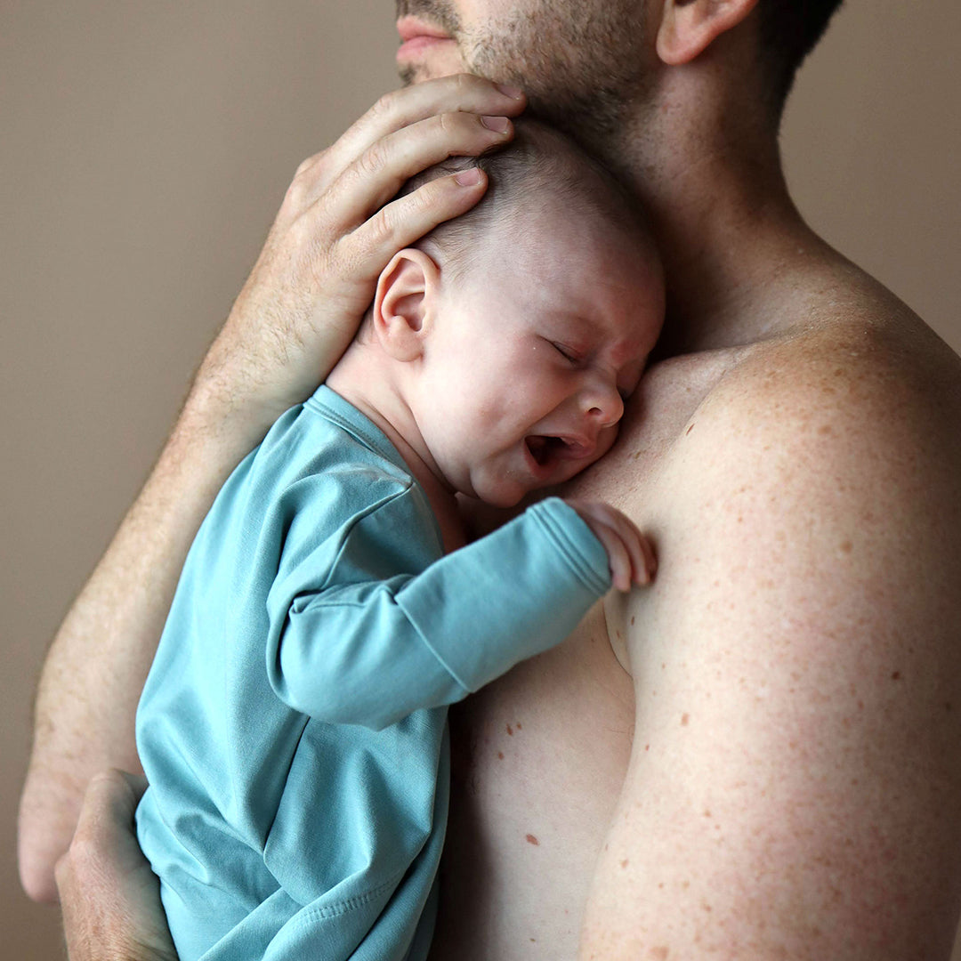 Man holding a sleeping baby in his arms with a neutral background