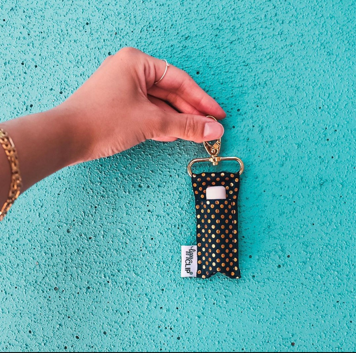 Hand holding a keychain with a polka dot design on a turquoise textured surface