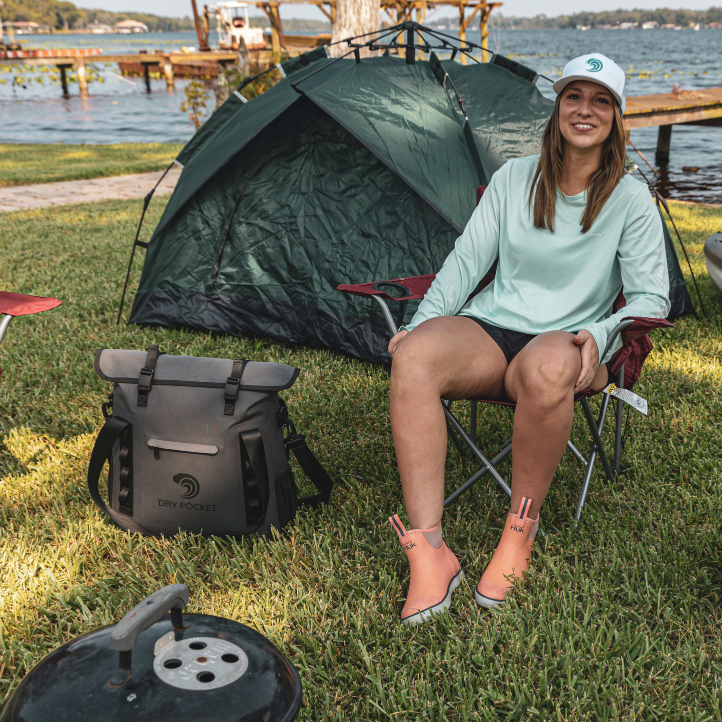 Waterproof floating tote cooler on grass, dark gray with front latch pocket and straps