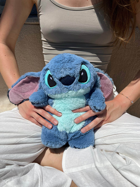 Blue plush hot water bottle held against abdomen, cartoon alien face with large ears