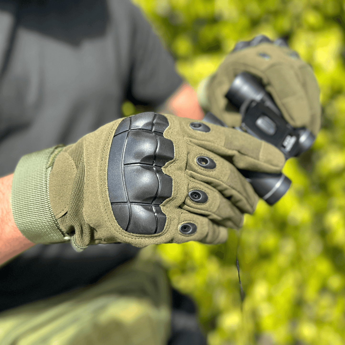 Tan tactical gloves on a hand, showing knuckle padding and stitched fingertip seams.