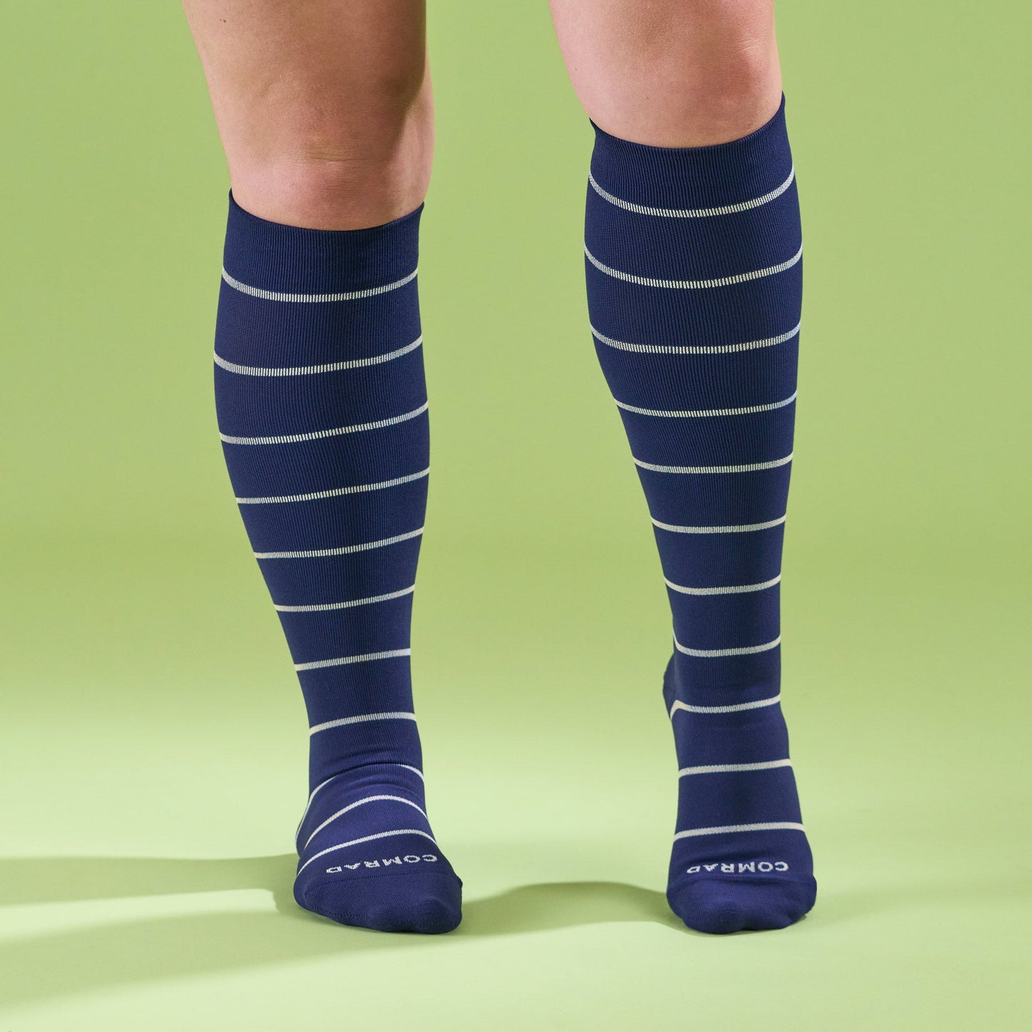 Knee-high compression socks on legs, navy blue with light stripe bands