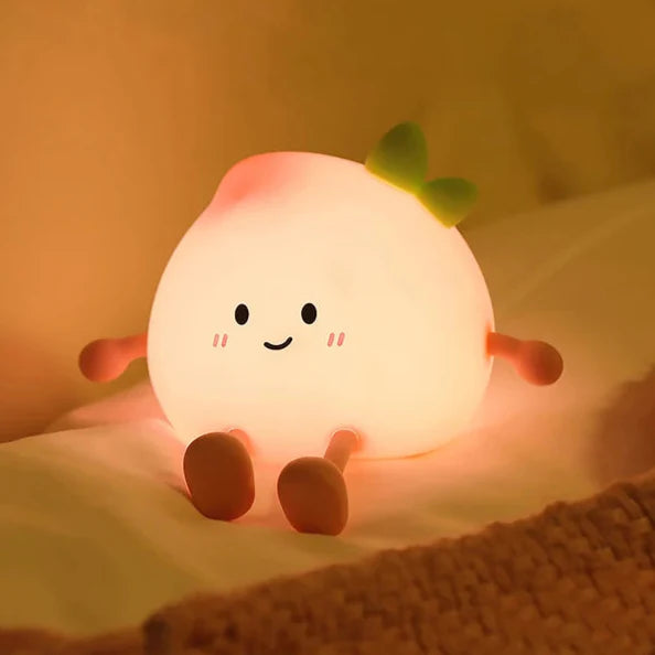 White peach-shaped night light with smiling face and green leaf, glowing softly