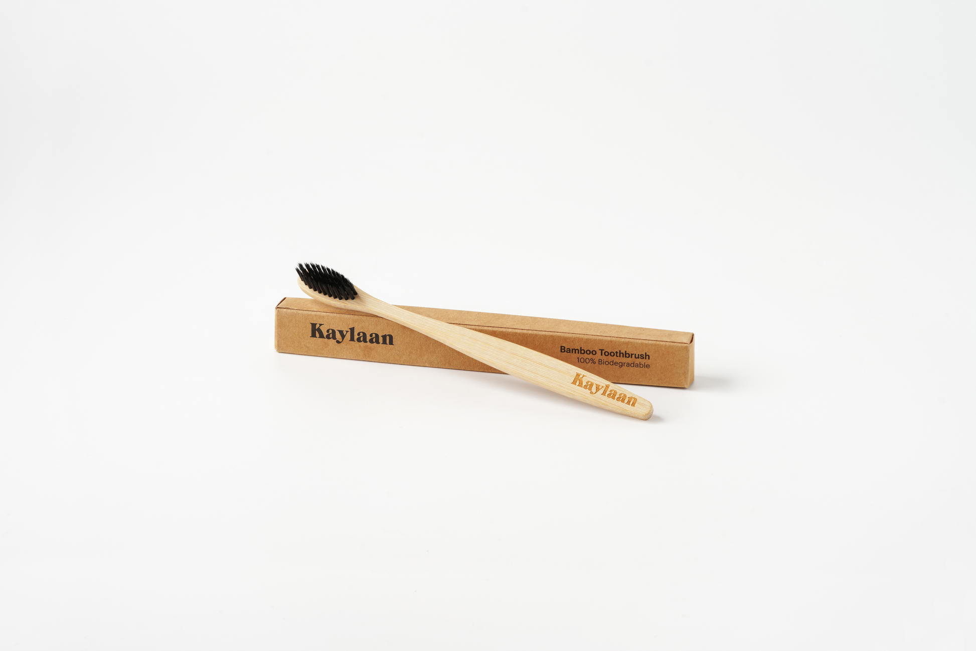 Kaylaan bamboo toothbrush with black bristles and light wood handle, plus kraft packaging