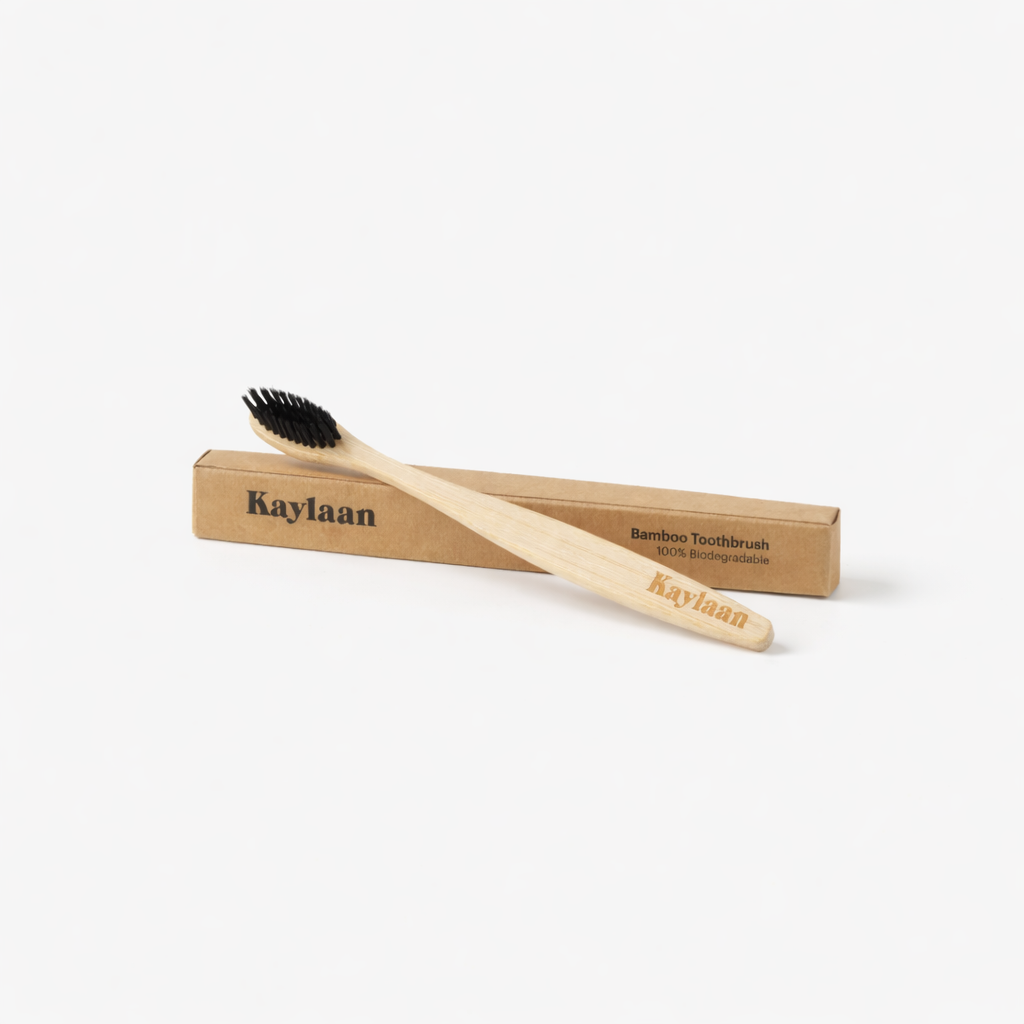 Kaylaan bamboo toothbrush with black bristles on light wood handle, shown with kraft sleeve