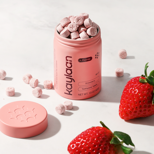 Fluoride strawberry toothpaste tablets in pink container with scattered tablet pieces
