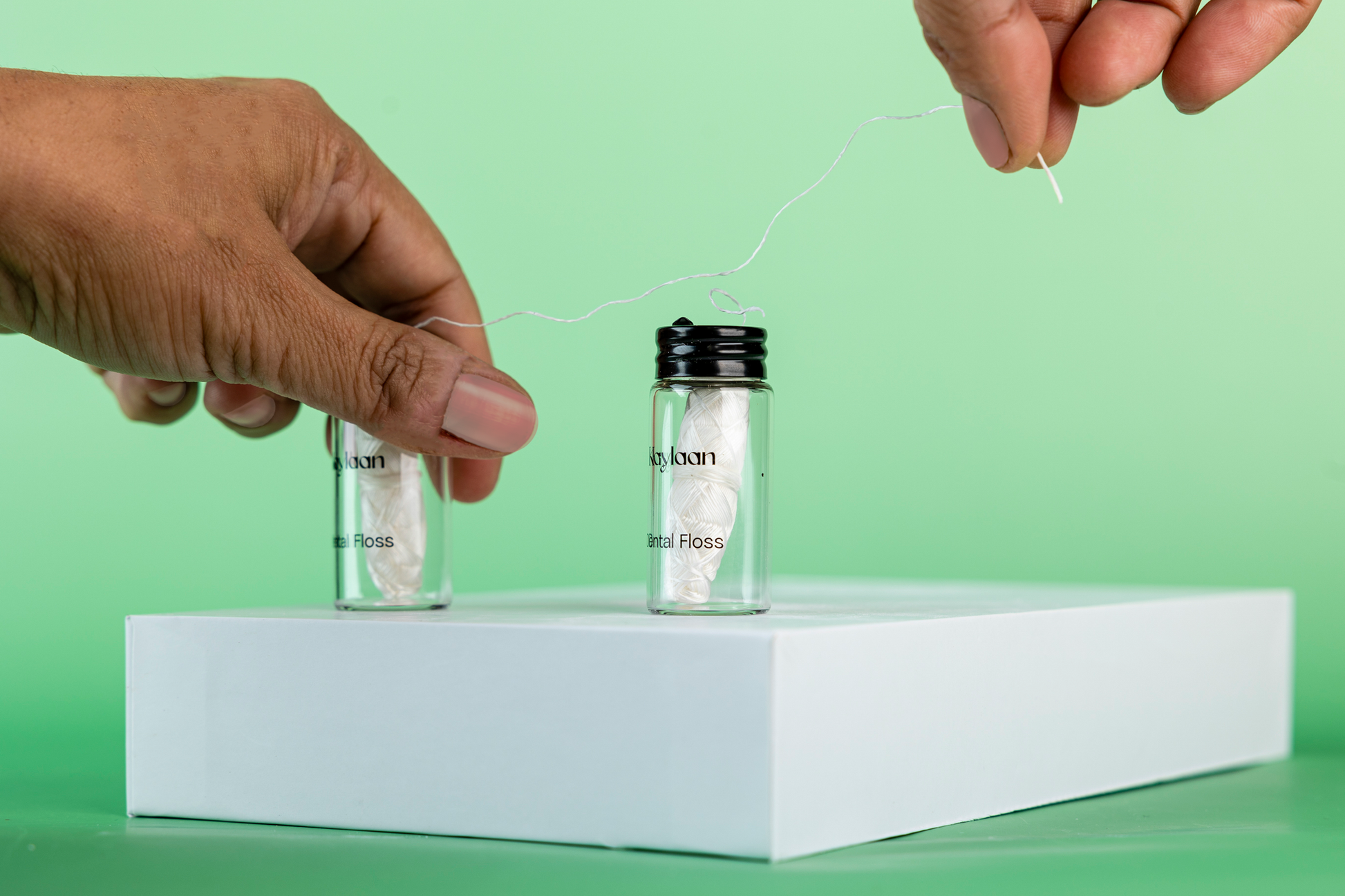 Hands pulling white dental floss from Kaylan bottle with another bottle nearby