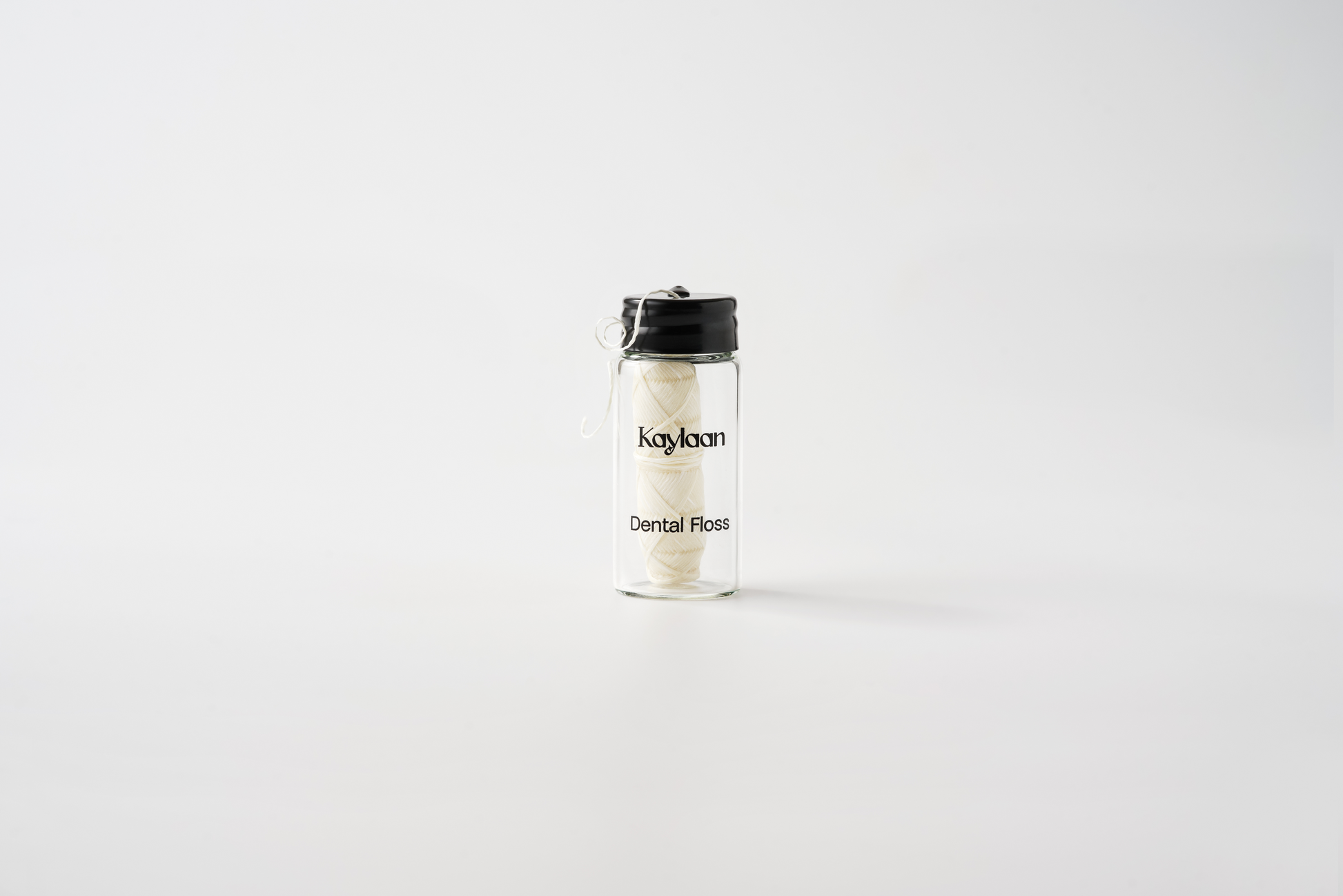 Dental floss bottle with clear glass and black cap, white floss strands inside