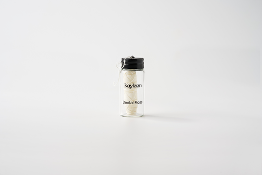 Dental floss bottle with clear glass and black cap, white floss strands inside