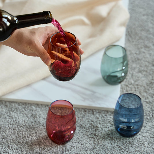 Hand pouring red wine into stemless acrylic wine glass with finger indent