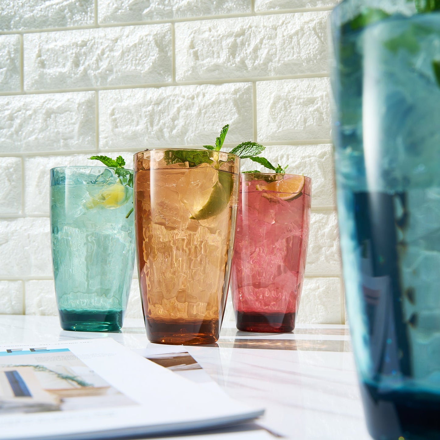 Three acrylic highball glasses—teal, orange, pink—with a partial blue glass