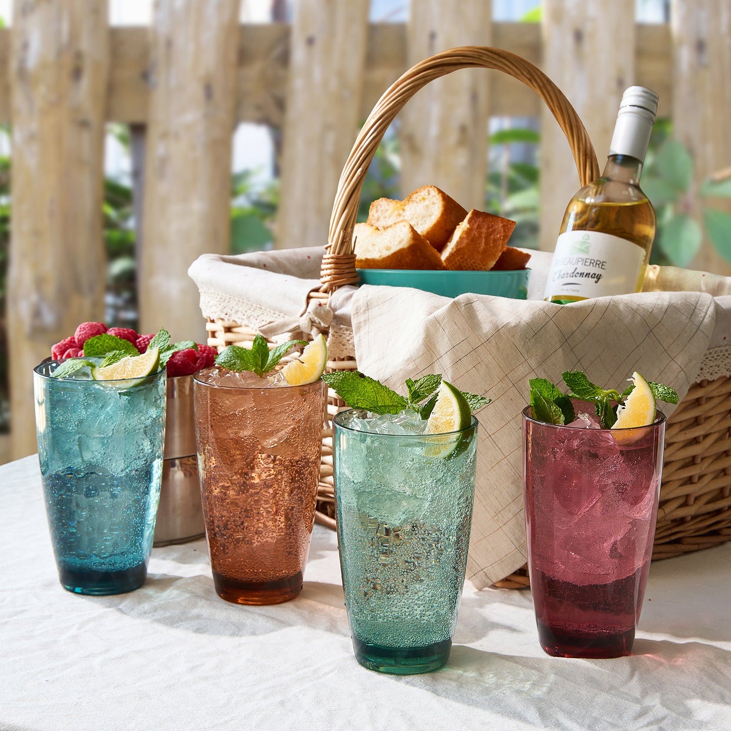 Four acrylic highball glasses in teal, bronze, mint, and berry with ice and herbs