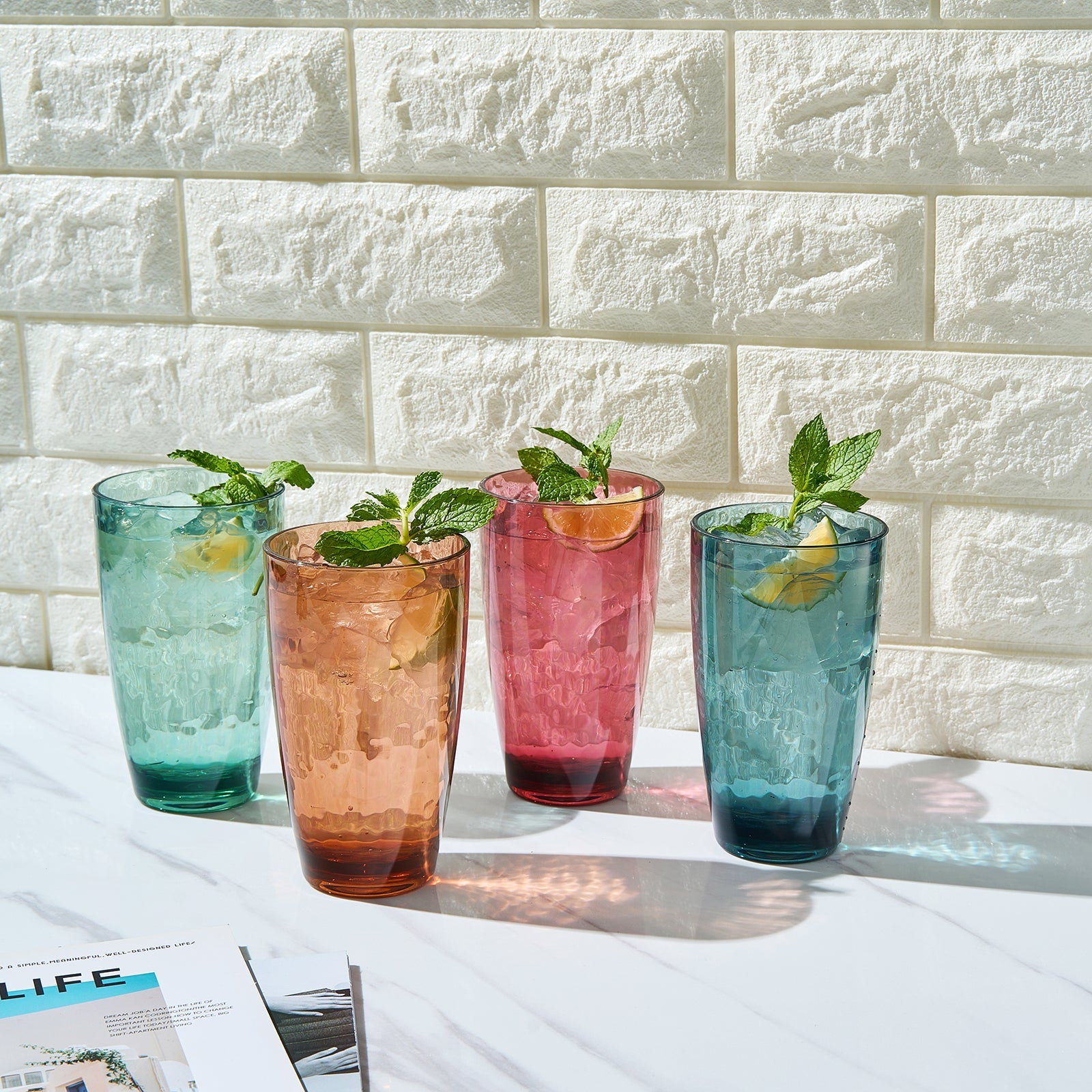 Four acrylic highball glasses with mint, orange, pink, and blue colors and herbs