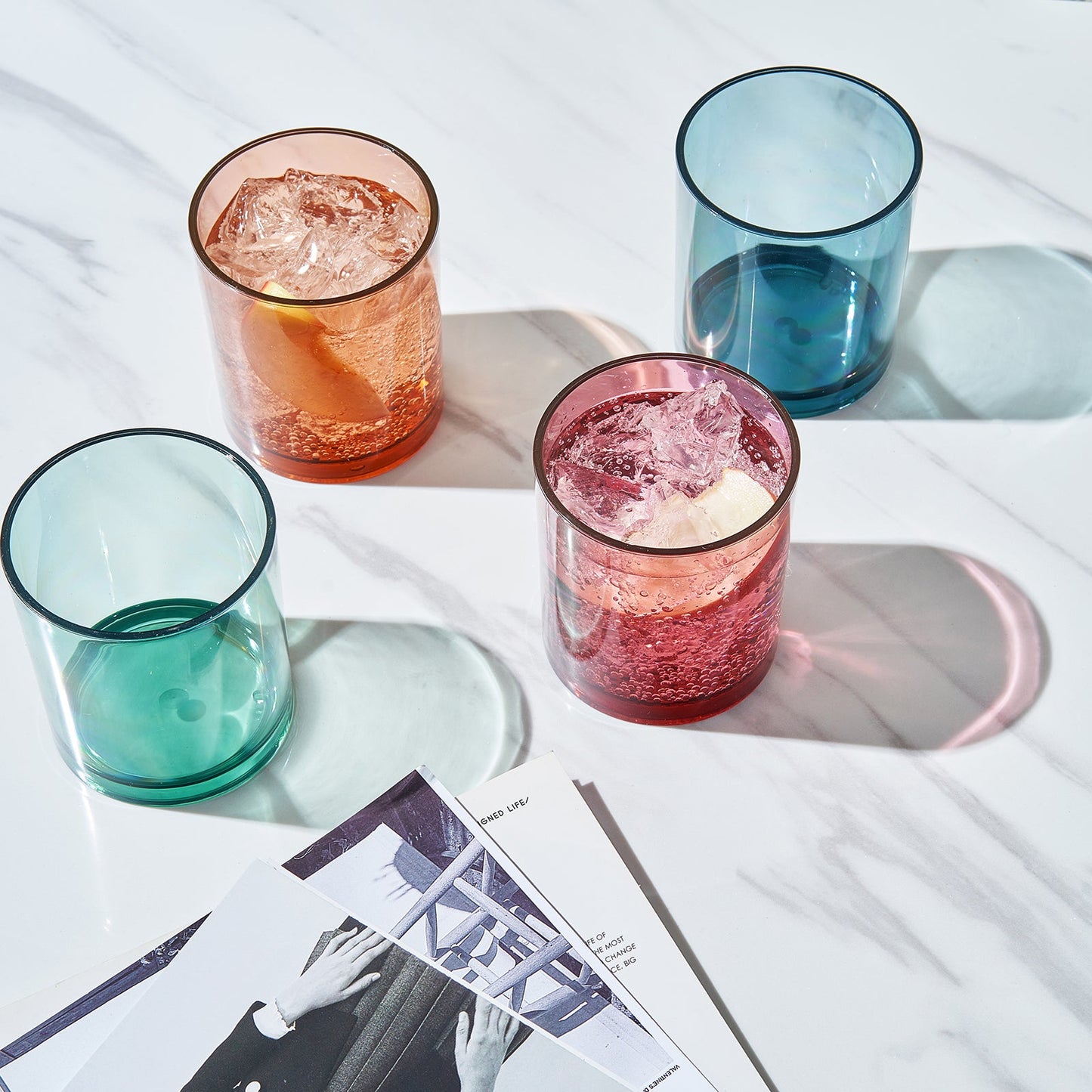 Acrylic lowball glasses with ice in amber, pink-red, teal, and blue colors