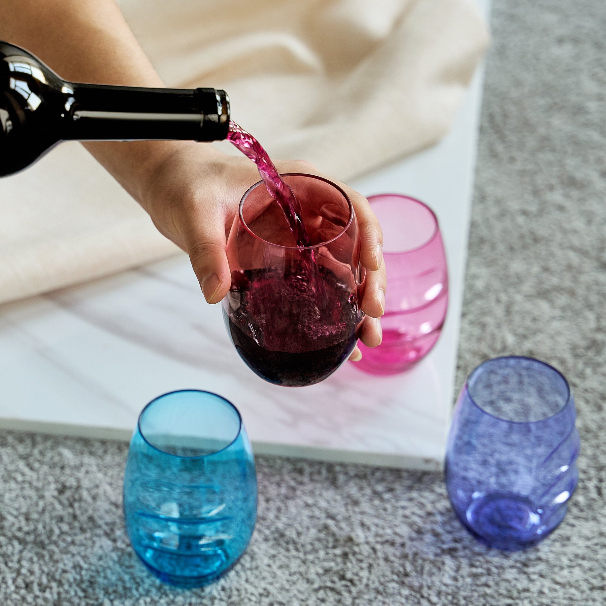 Pouring wine into an acrylic stemless wine glass with finger-indented sides; blue and purple