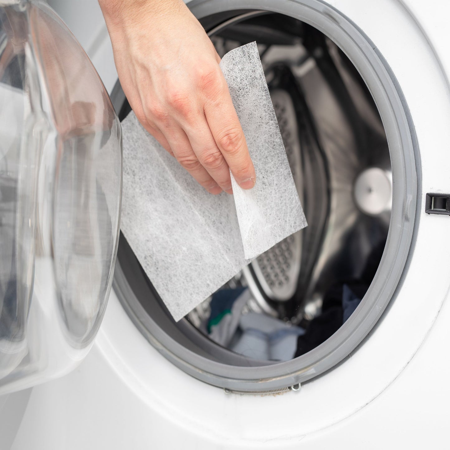 Hand placing a white laundry detergent sheet into a front-loading washer drum